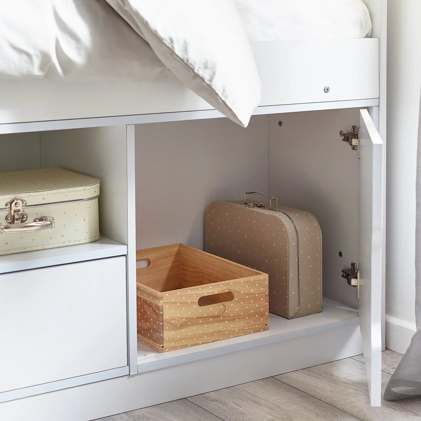 White low sleeper bed with open storage compartment, wooden box, and suitcases