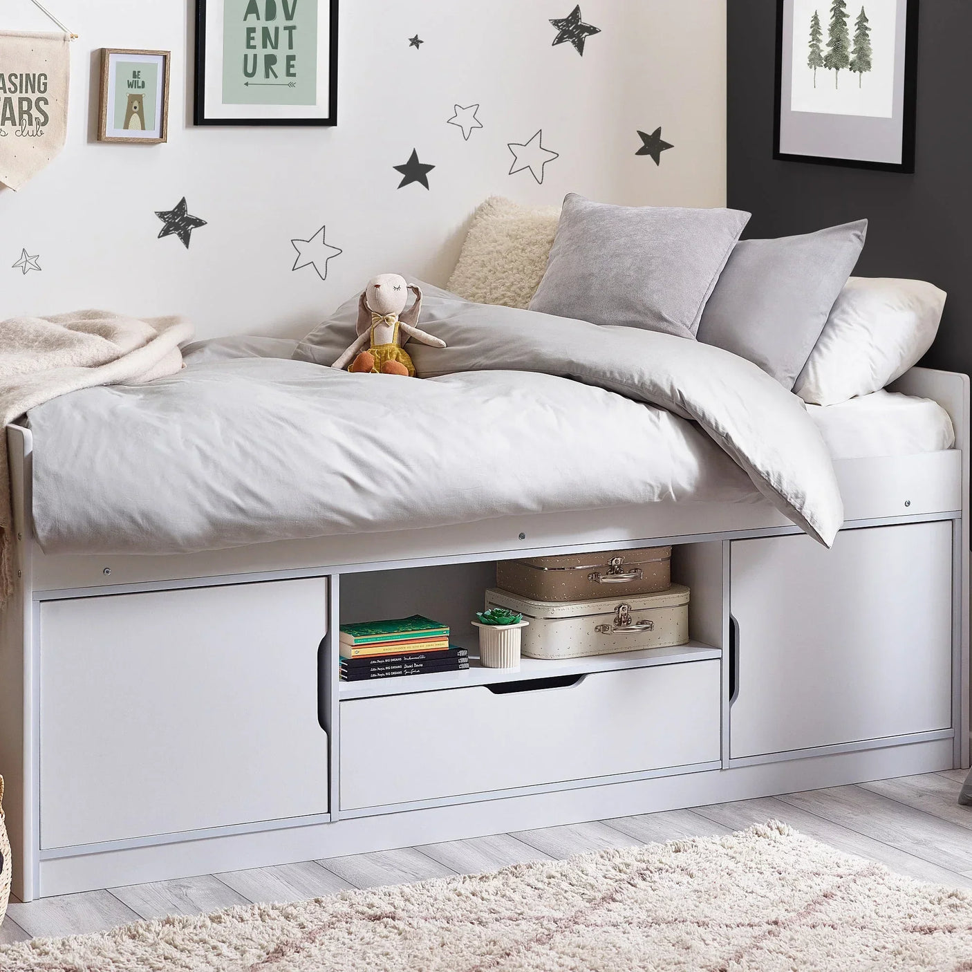 White low sleeper bed with storage drawers, shelves, and soft bedding in a kids' room