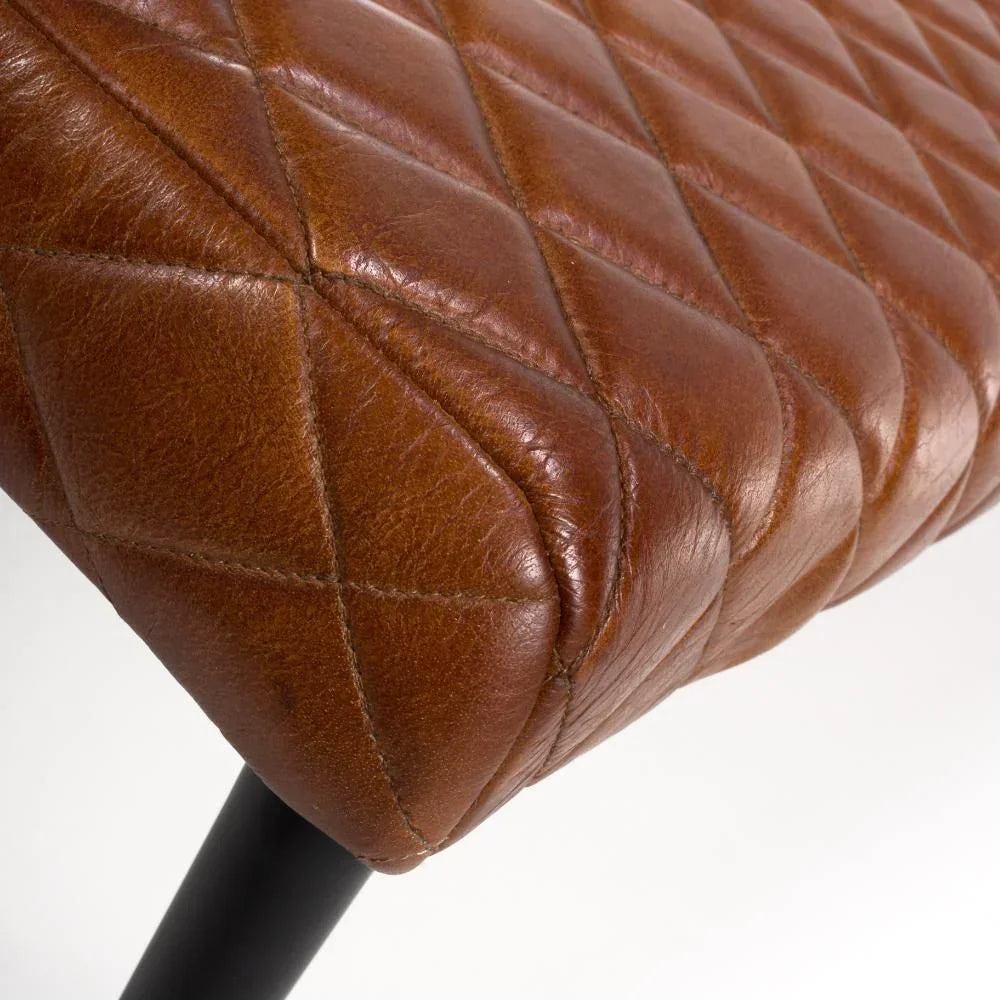 Close-up of brown leather dining chair seat with diamond quilted stitching and black leg