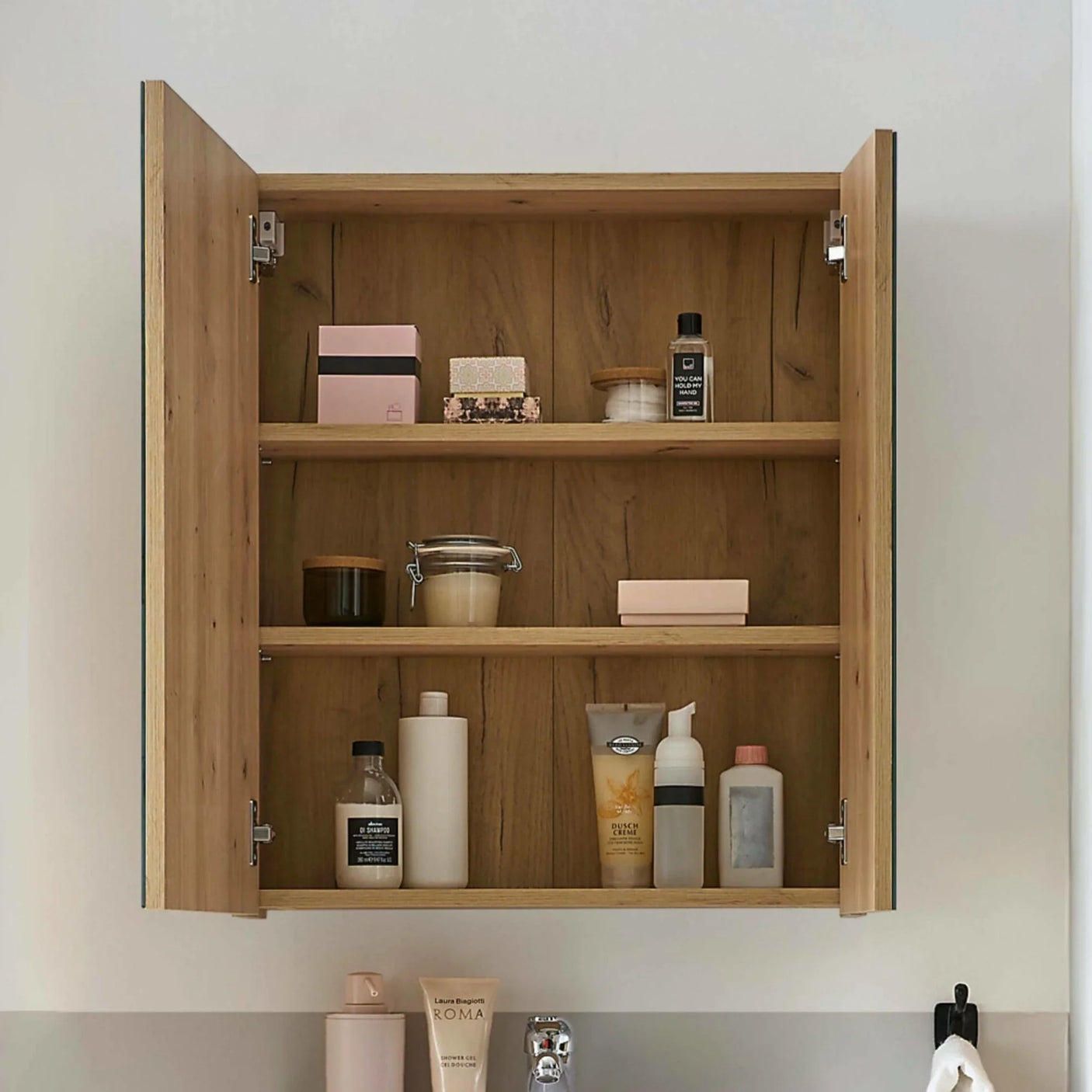 Wooden bathroom cabinet with open doors showing shelves of toiletries and bottles