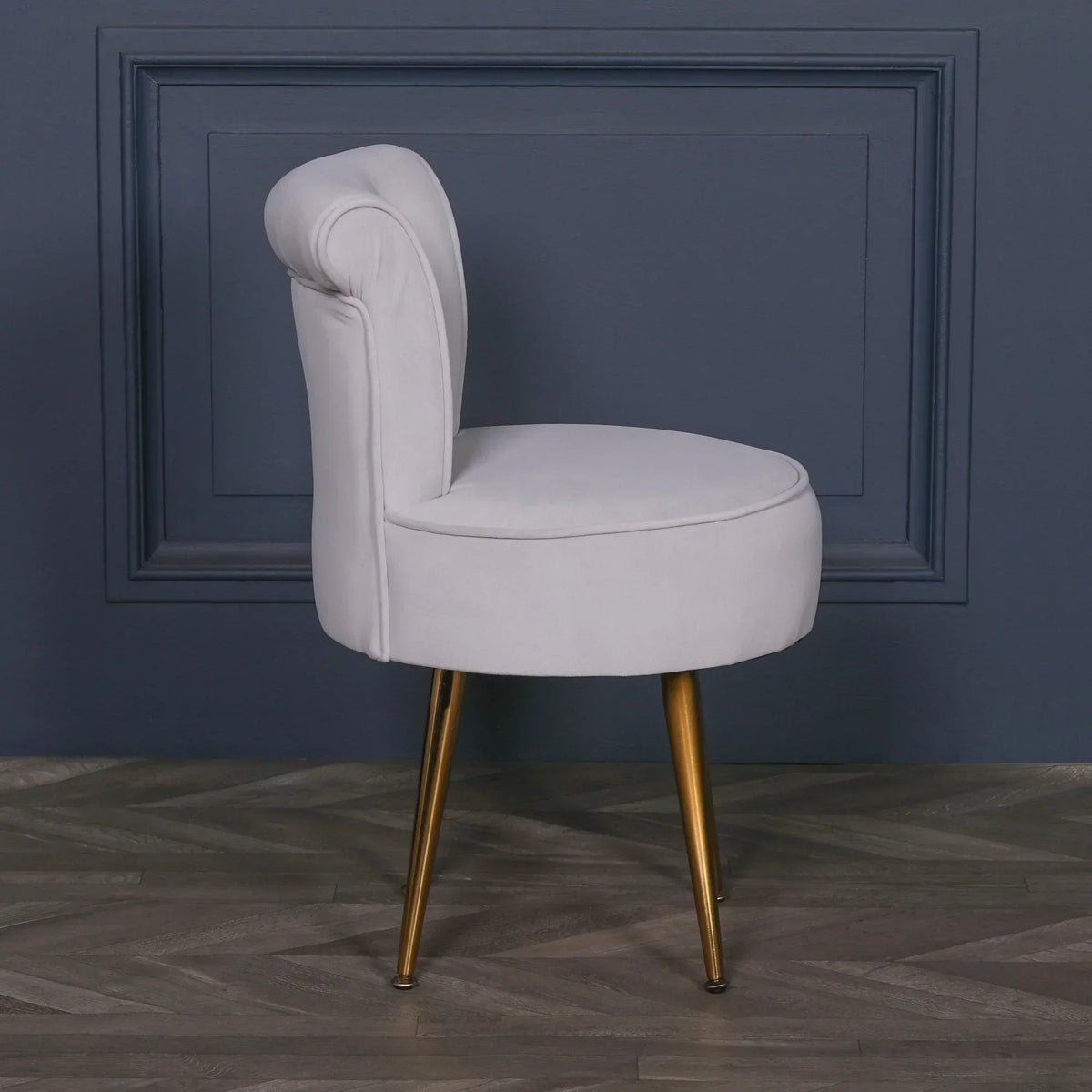 Light grey velvet accent chair with gold legs side view against blue wall