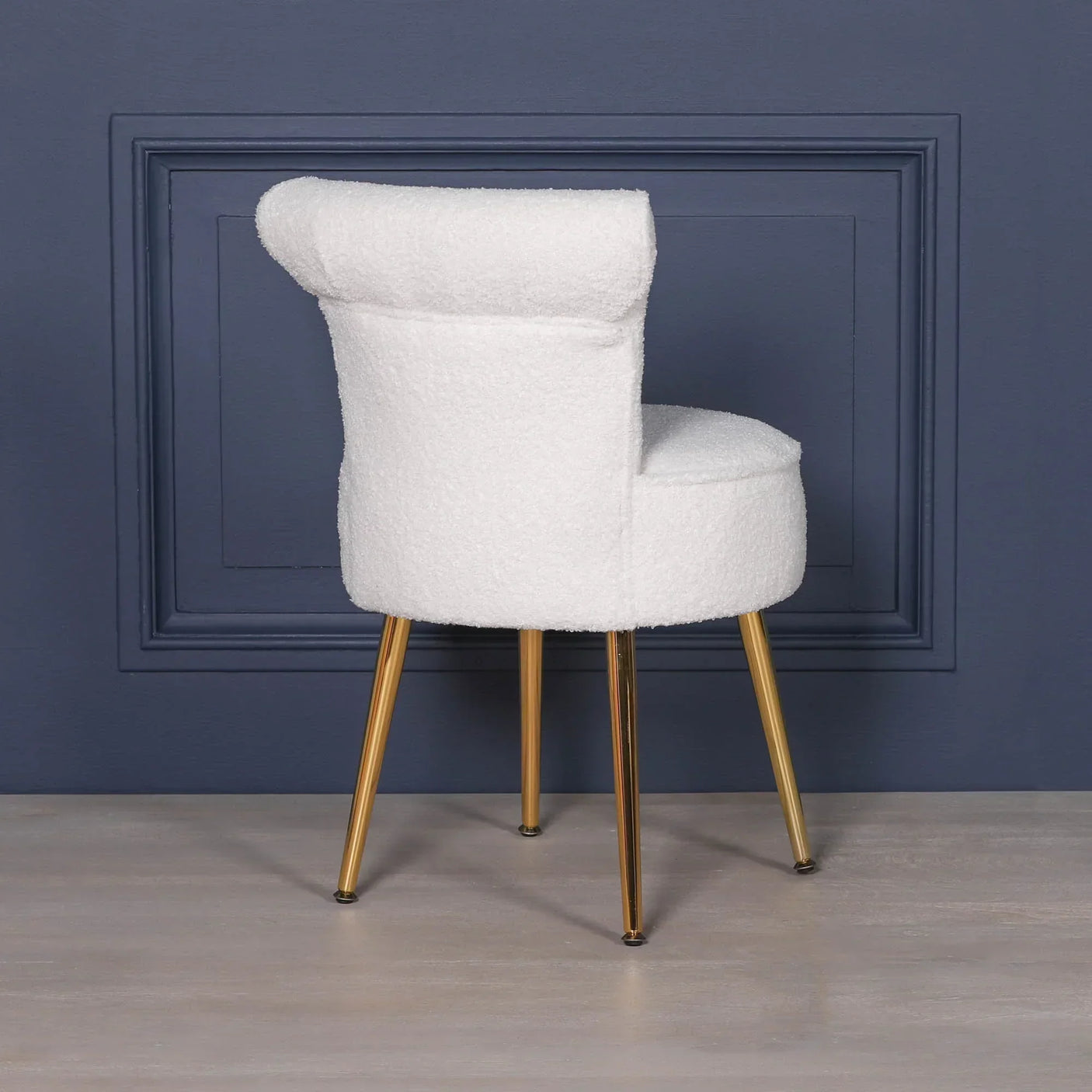 White boucle accent chair with gold metal legs against navy blue wall