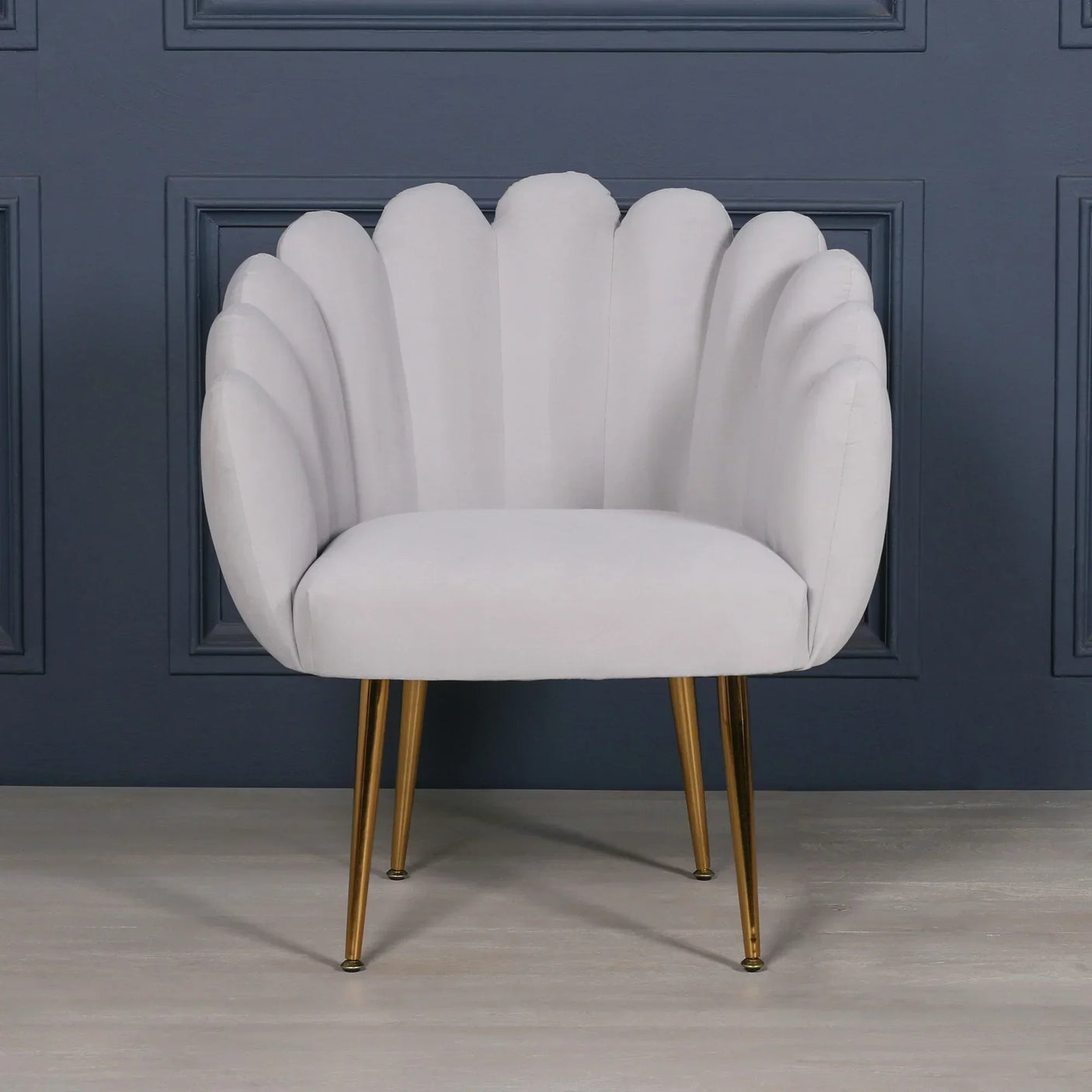 Grey accent chair with scalloped velvet backrest and gold metal legs against blue panel wall