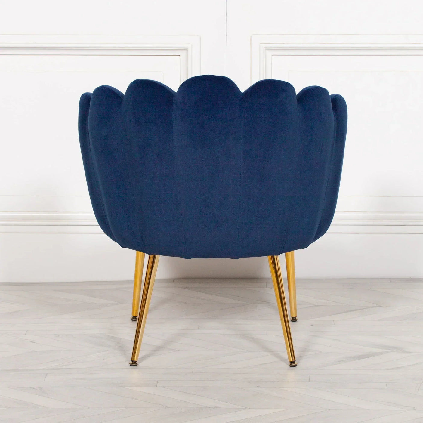 Blue velvet accent chair with gold legs, scalloped back design, rear view on wood floor