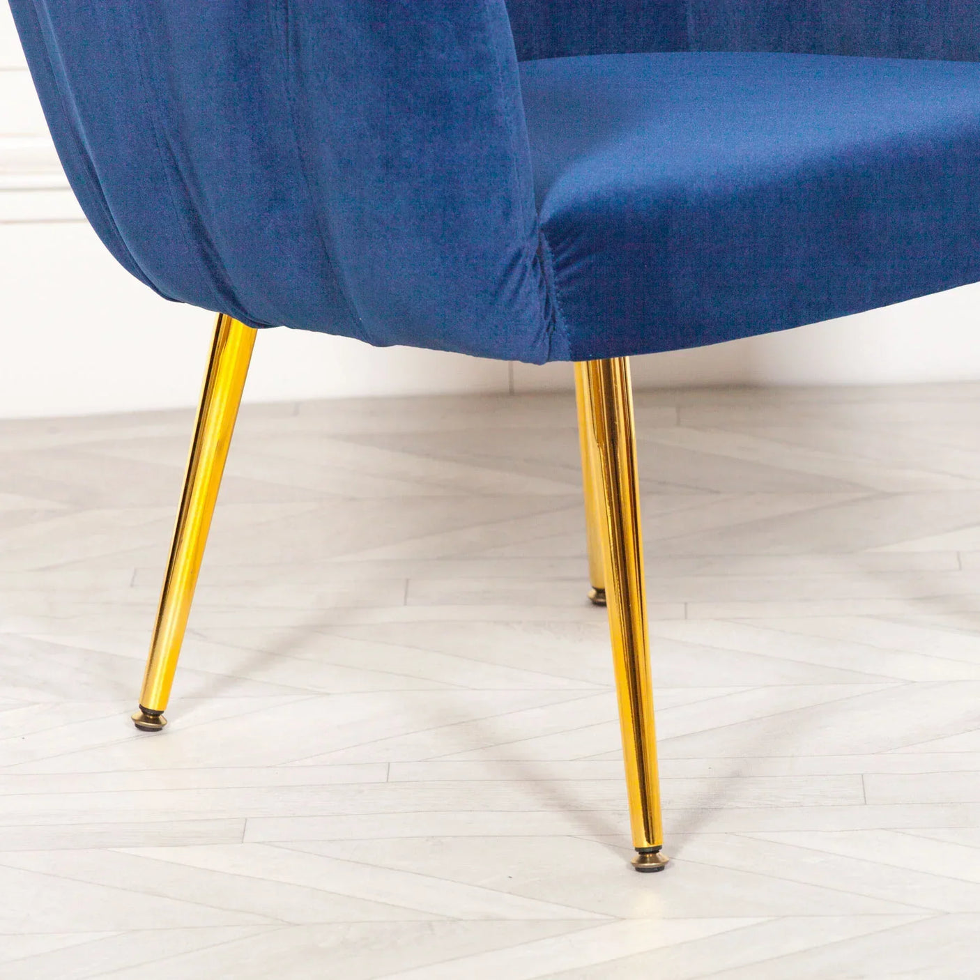 Blue velvet accent chair with gold metal legs on light herringbone floor