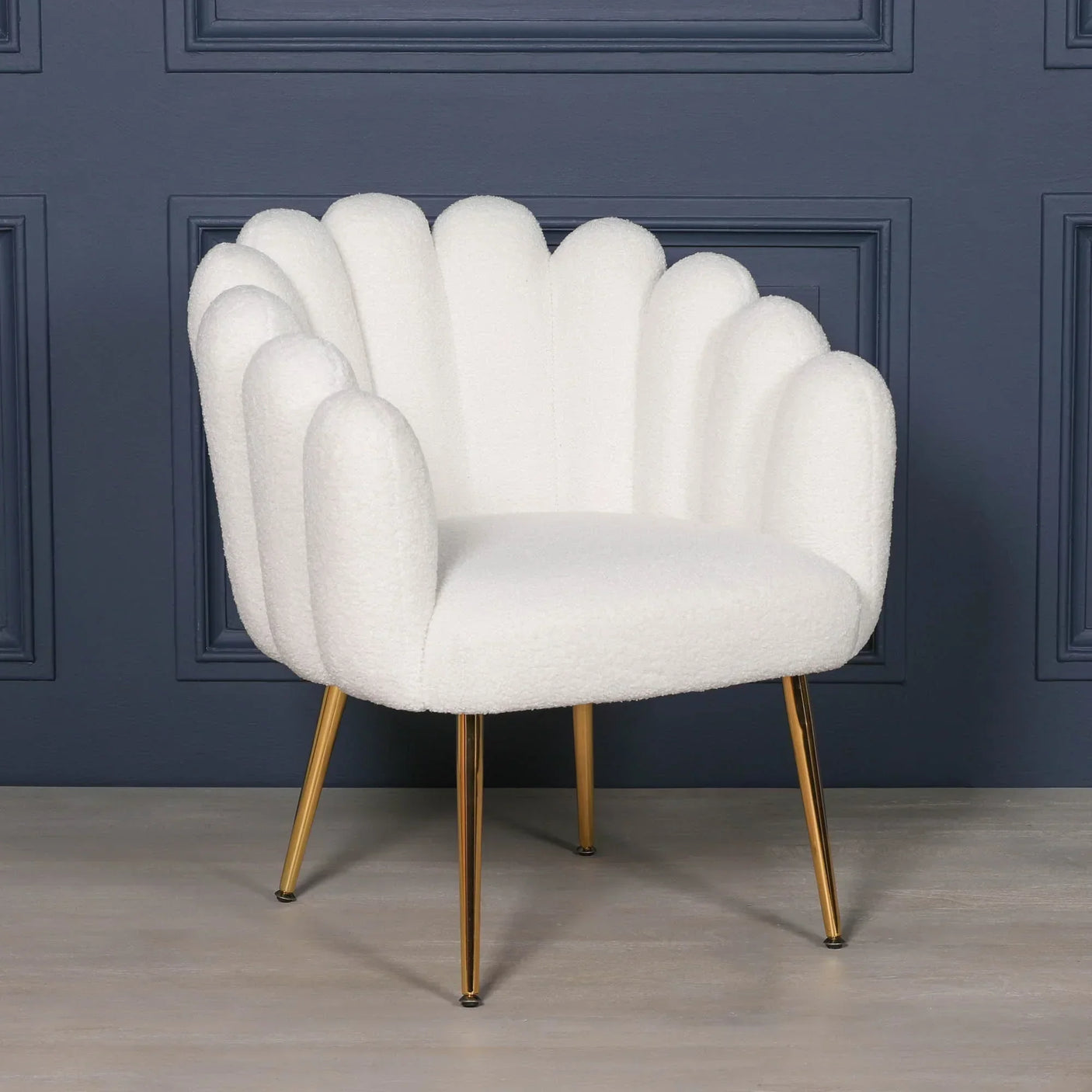 White bouclé accent chair with gold legs and scalloped backrest against navy wall