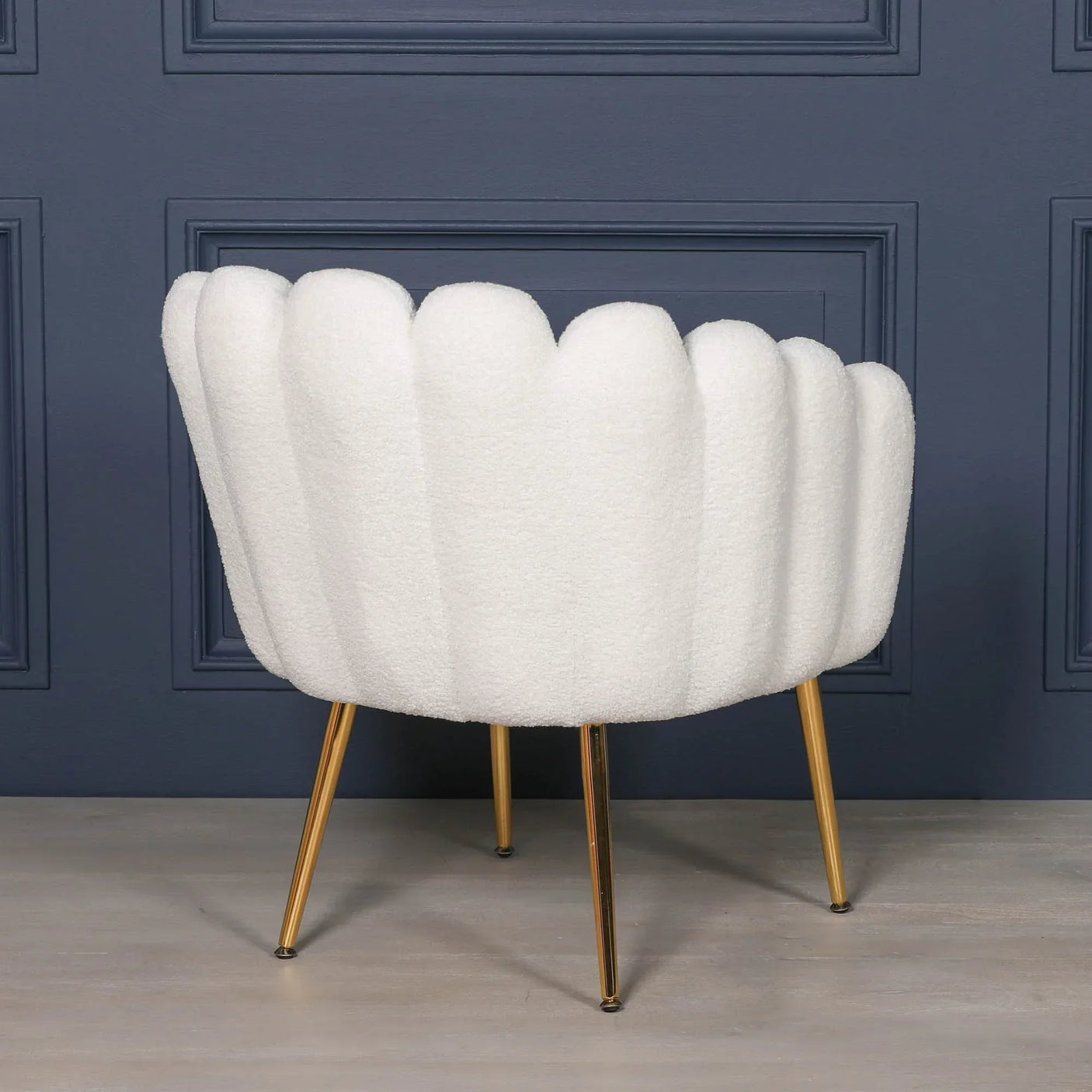 White boucle accent chair with gold legs in front of dark panelled wall