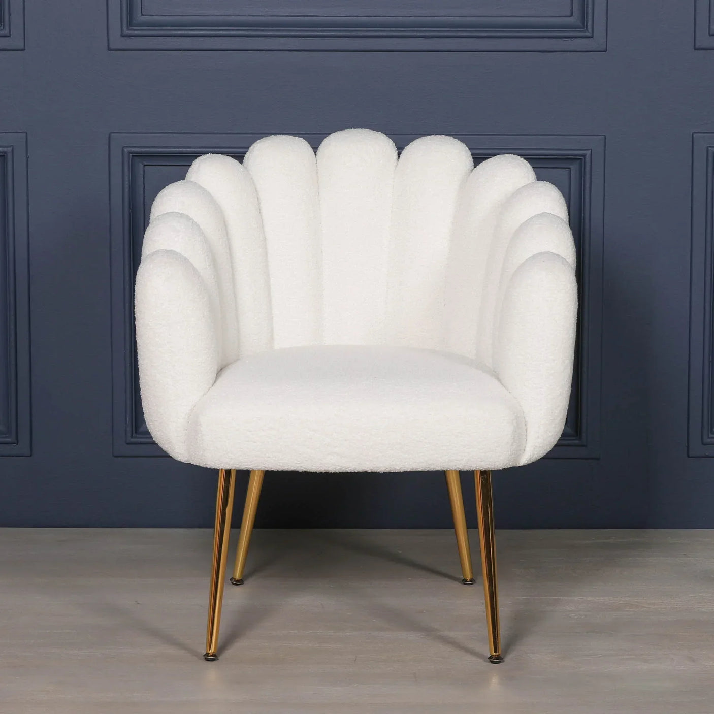 White boucle accent chair with scalloped backrest and gold metal legs against dark wall
