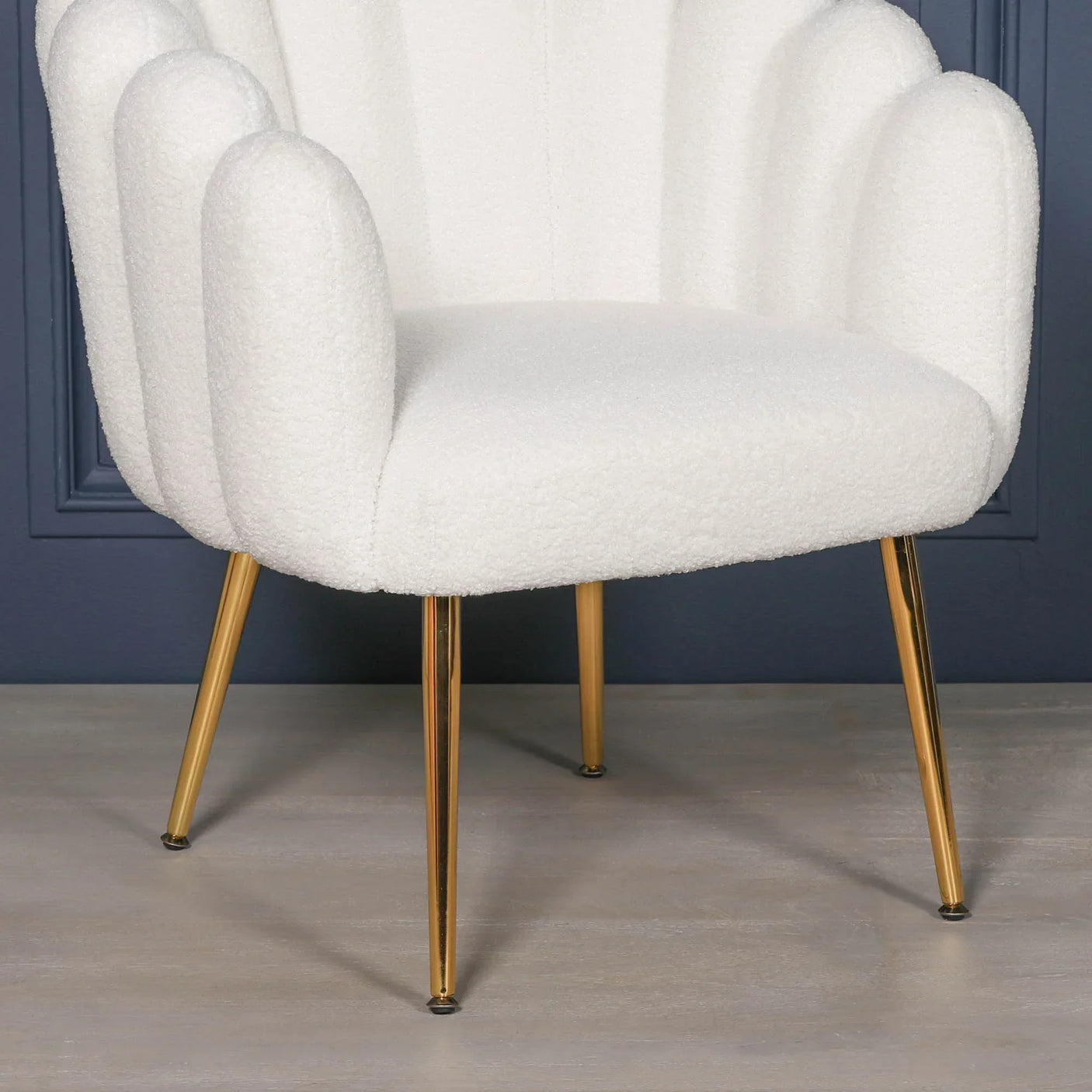 White accent chair with textured upholstery and gold legs on wooden floor