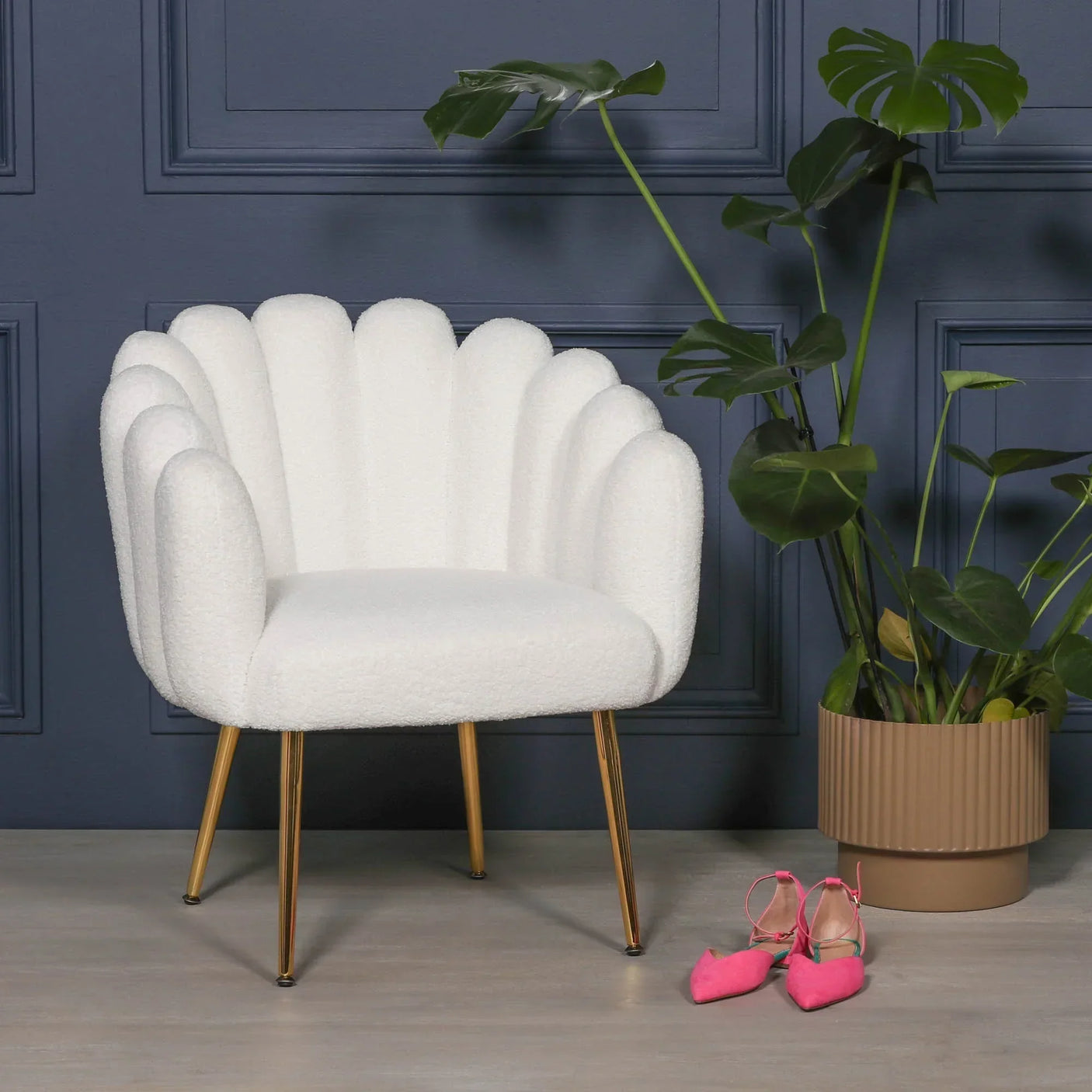 White scalloped accent chair with gold legs beside plant and pink shoes on grey floor