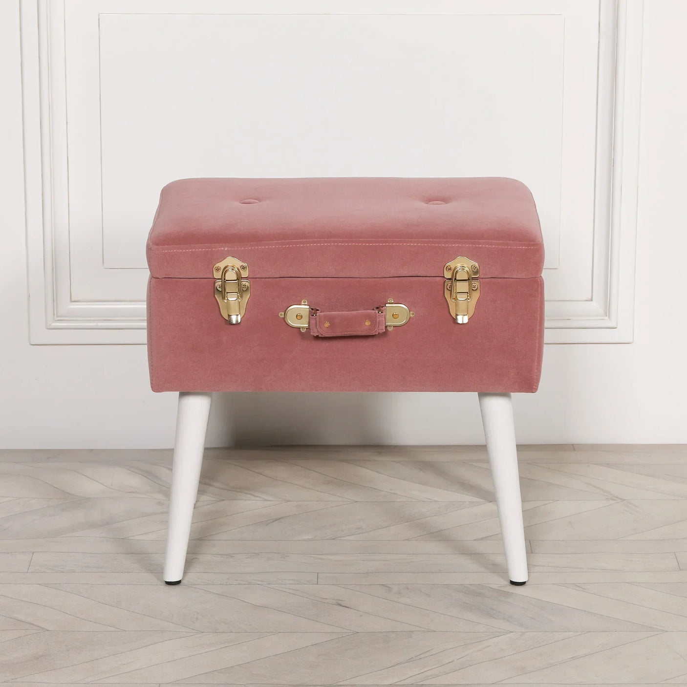 Pink velvet storage bench with gold clasps and white legs on wooden floor