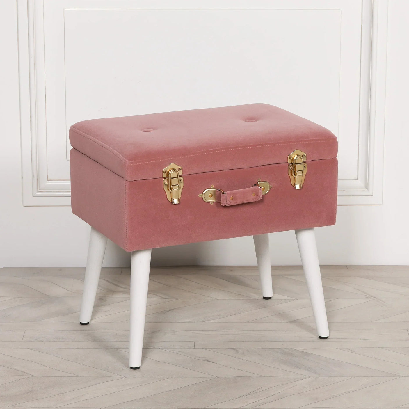 Pink velvet storage bench with gold clasps and white tapered legs on wooden floor