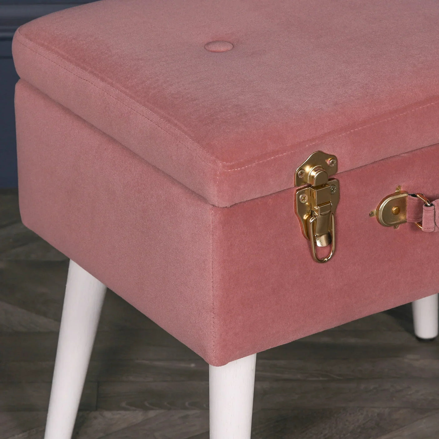 Pink velvet storage bench with gold latch detail and white wooden legs on wood floor