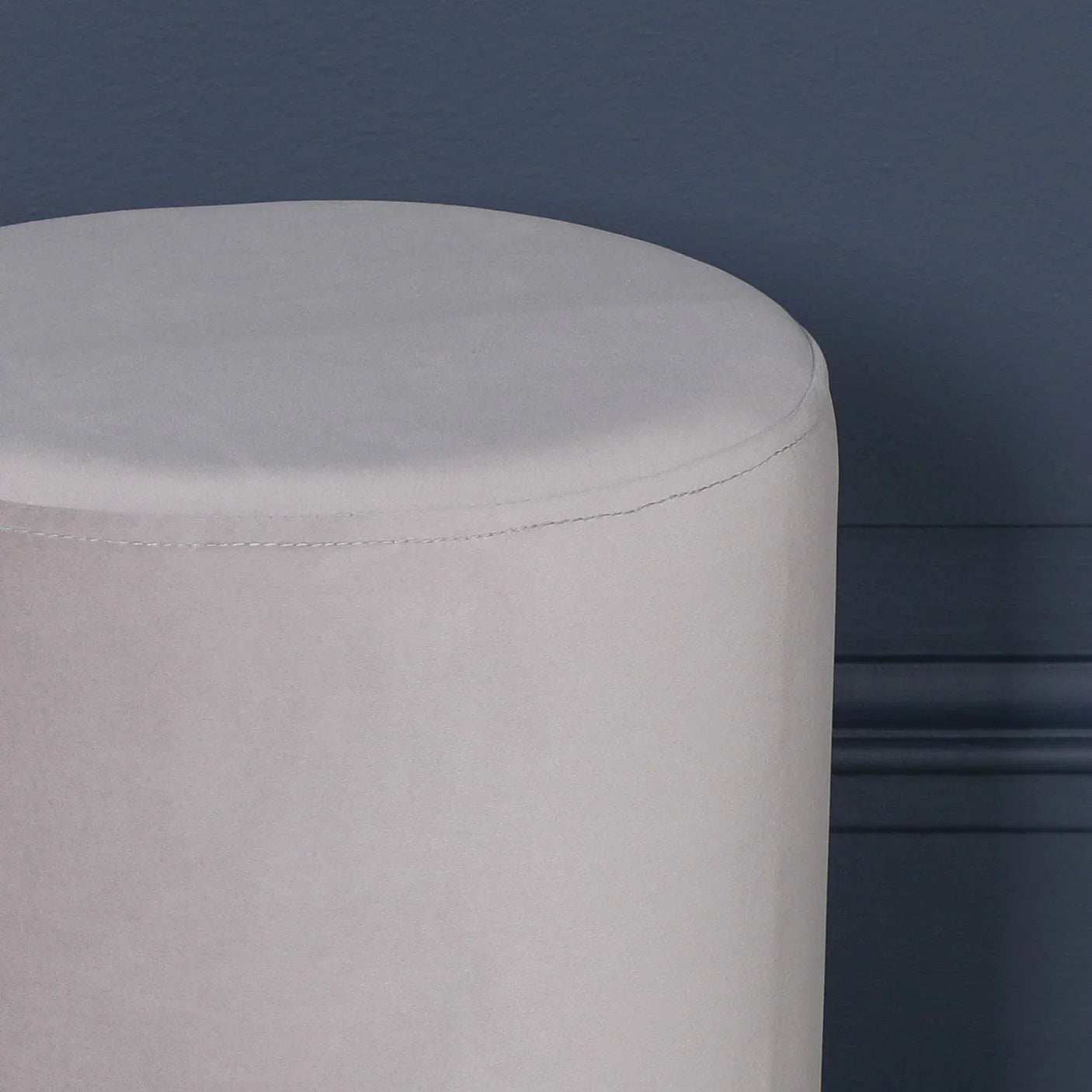 Light grey velvet round stool against dark blue wall