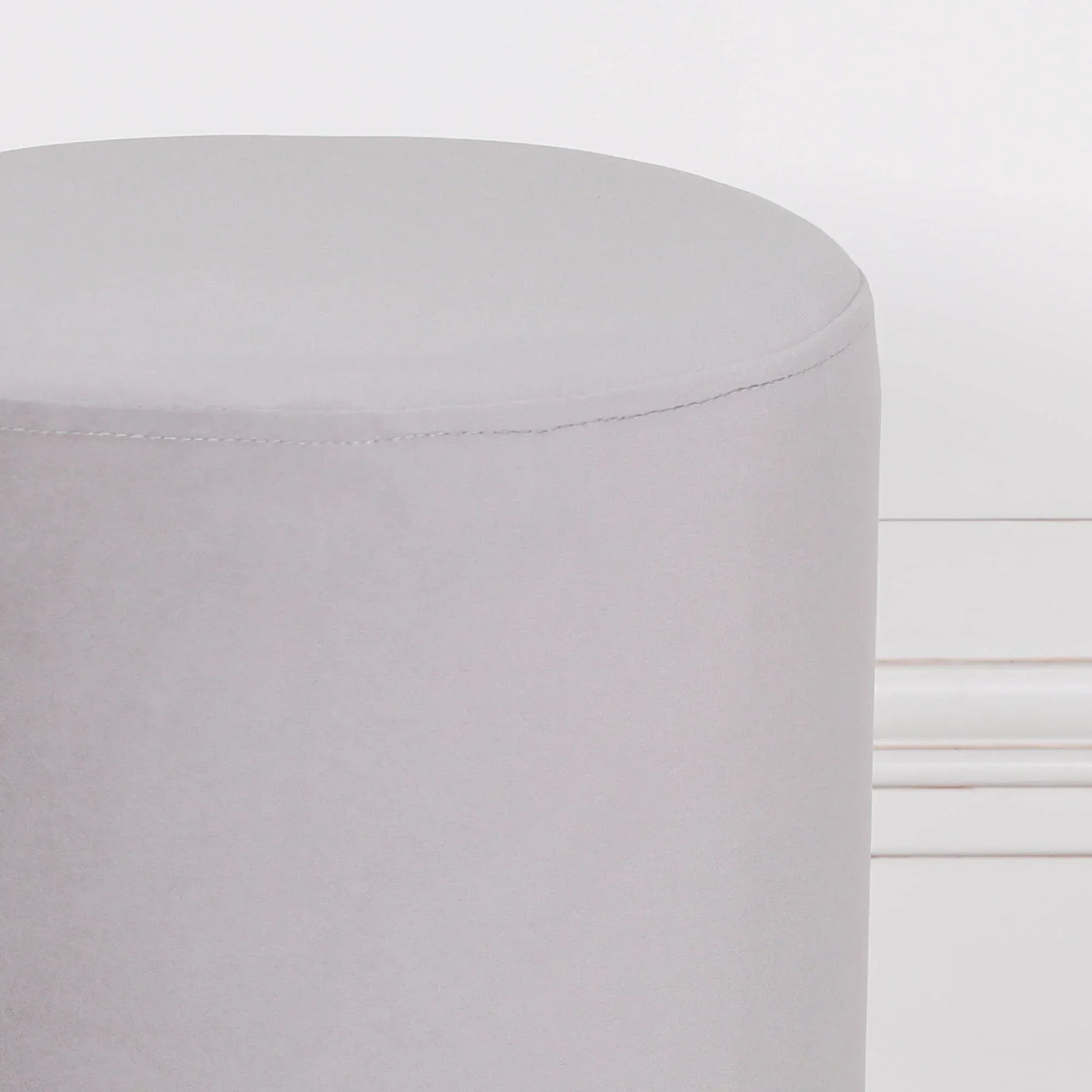 Light grey velvet ottoman stool with round shape placed against white wall
