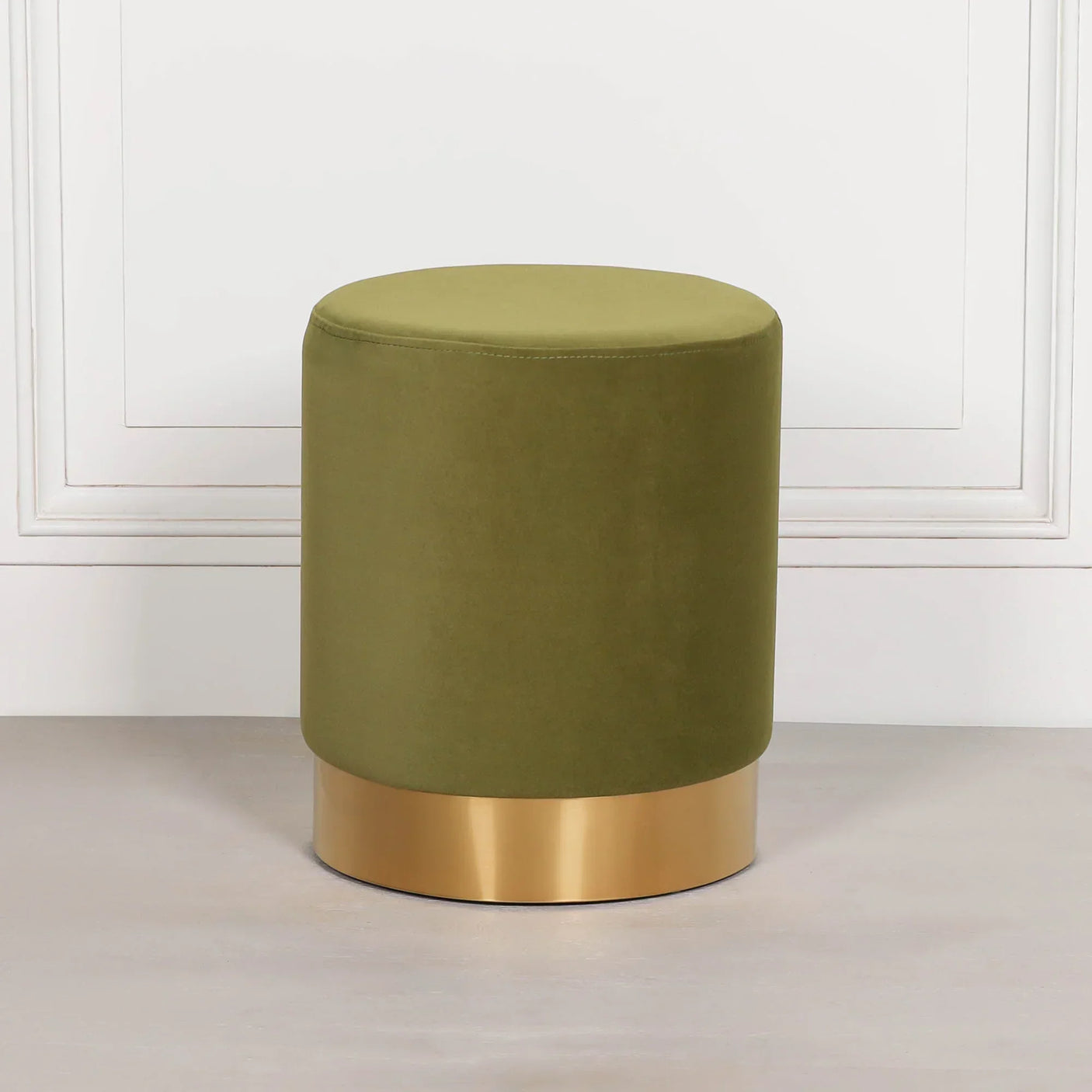 Green velvet ottoman stool with gold metal base against white wall