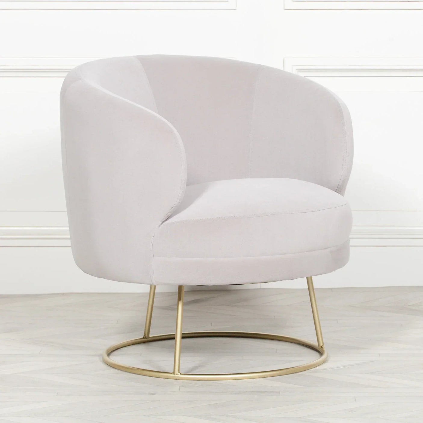 Light grey velvet accent chair with rounded back and gold metal base on wooden floor