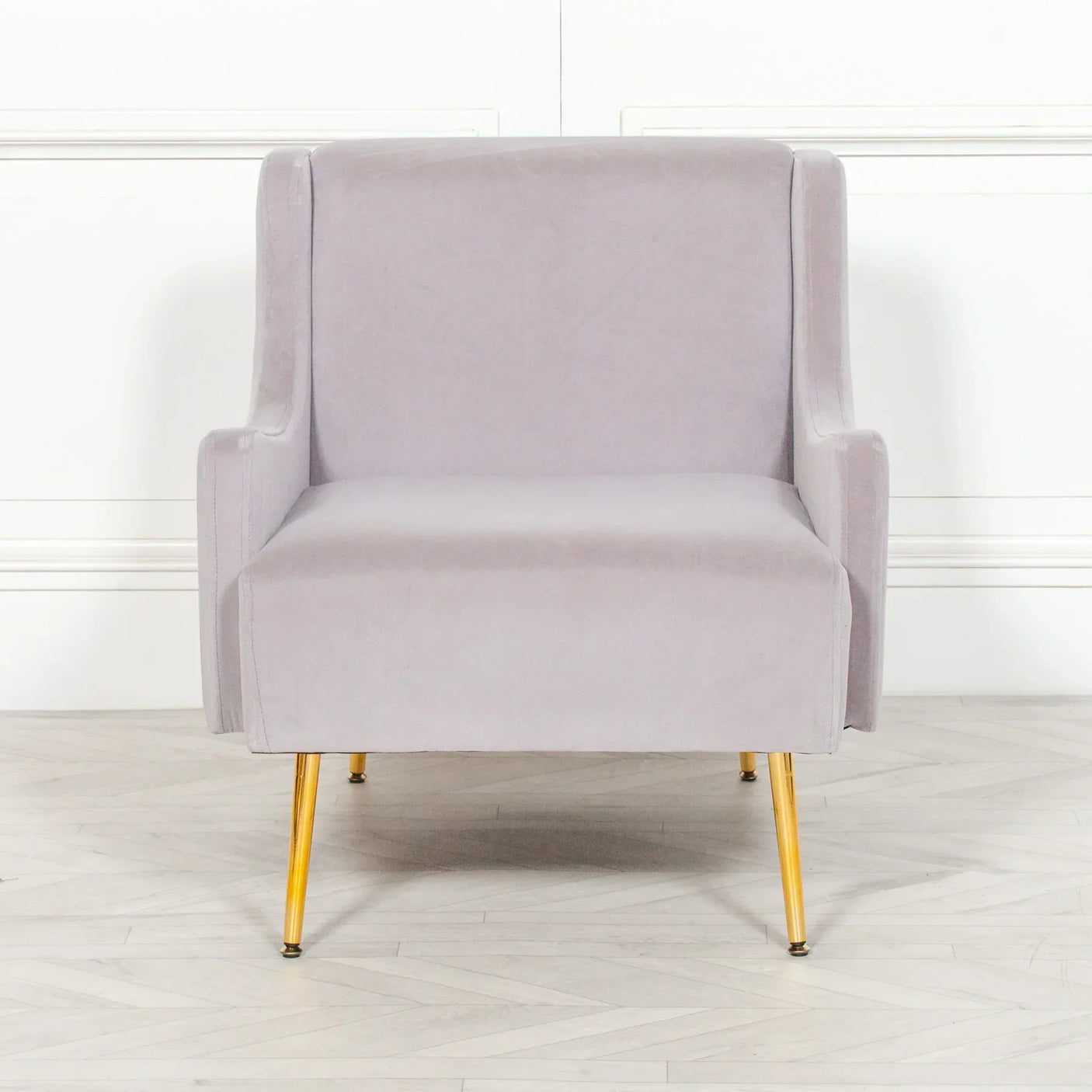 Light grey velvet armchair with gold metal legs on wooden floor, front view