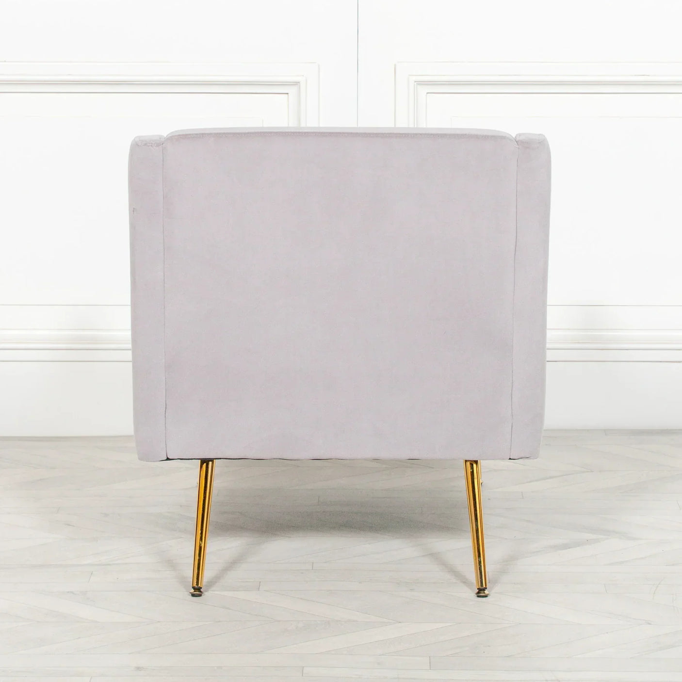 Back view of grey velvet armchair with gold metal legs on light wood floor