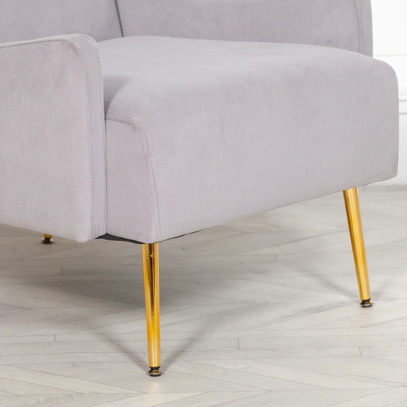 Grey velvet armchair with slim gold metal legs on light herringbone floor