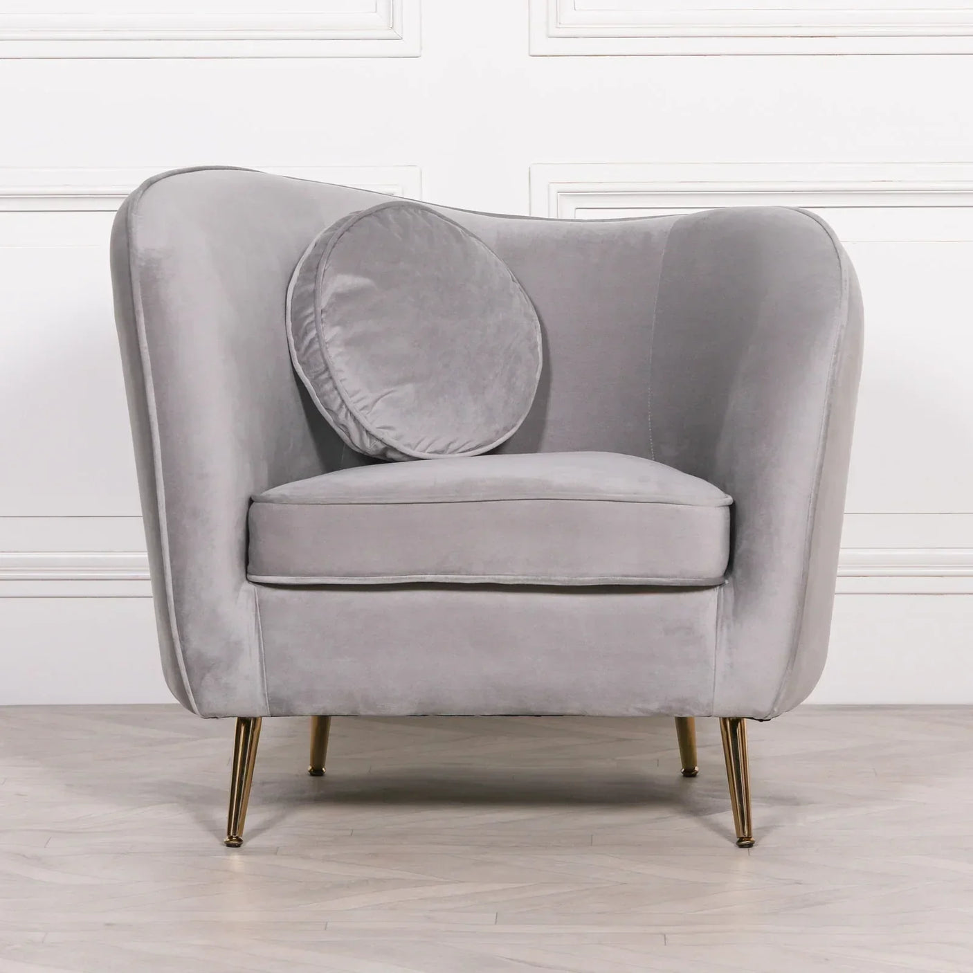 Grey velvet accent chair with gold legs and round cushion on wood floor