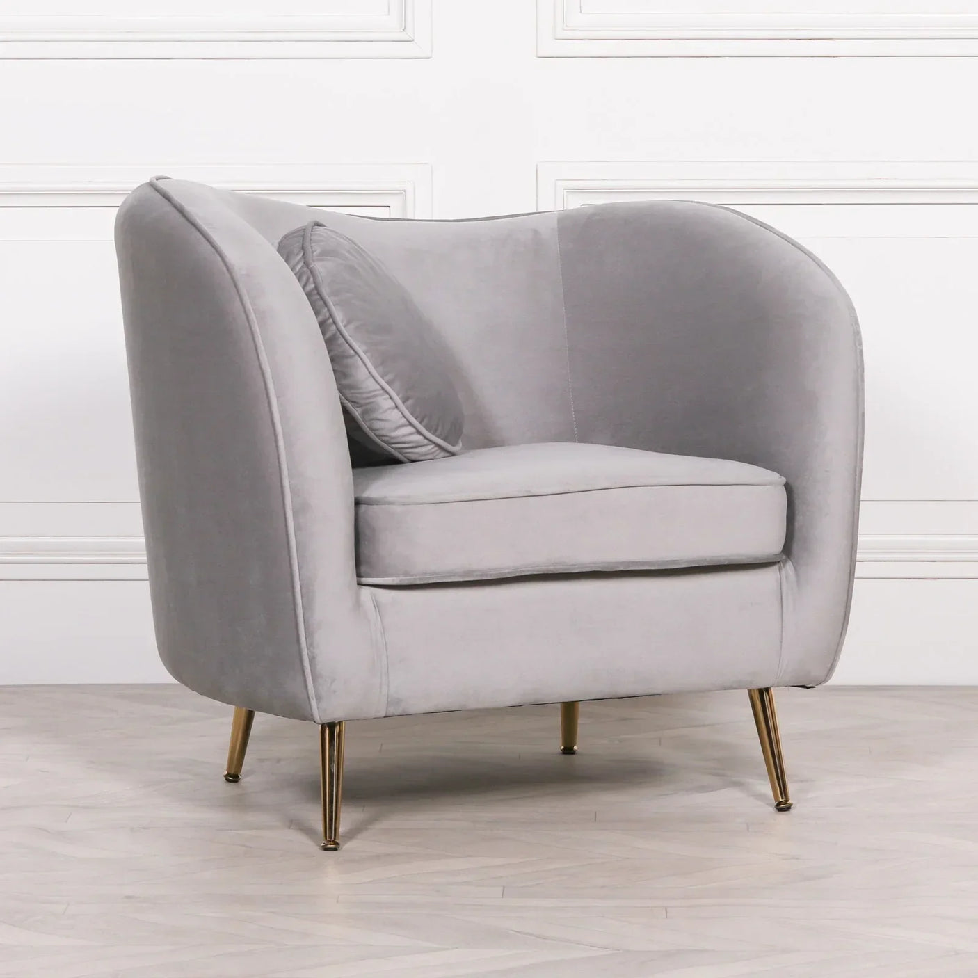 Grey velvet armchair with gold legs and cushion against white panel wall