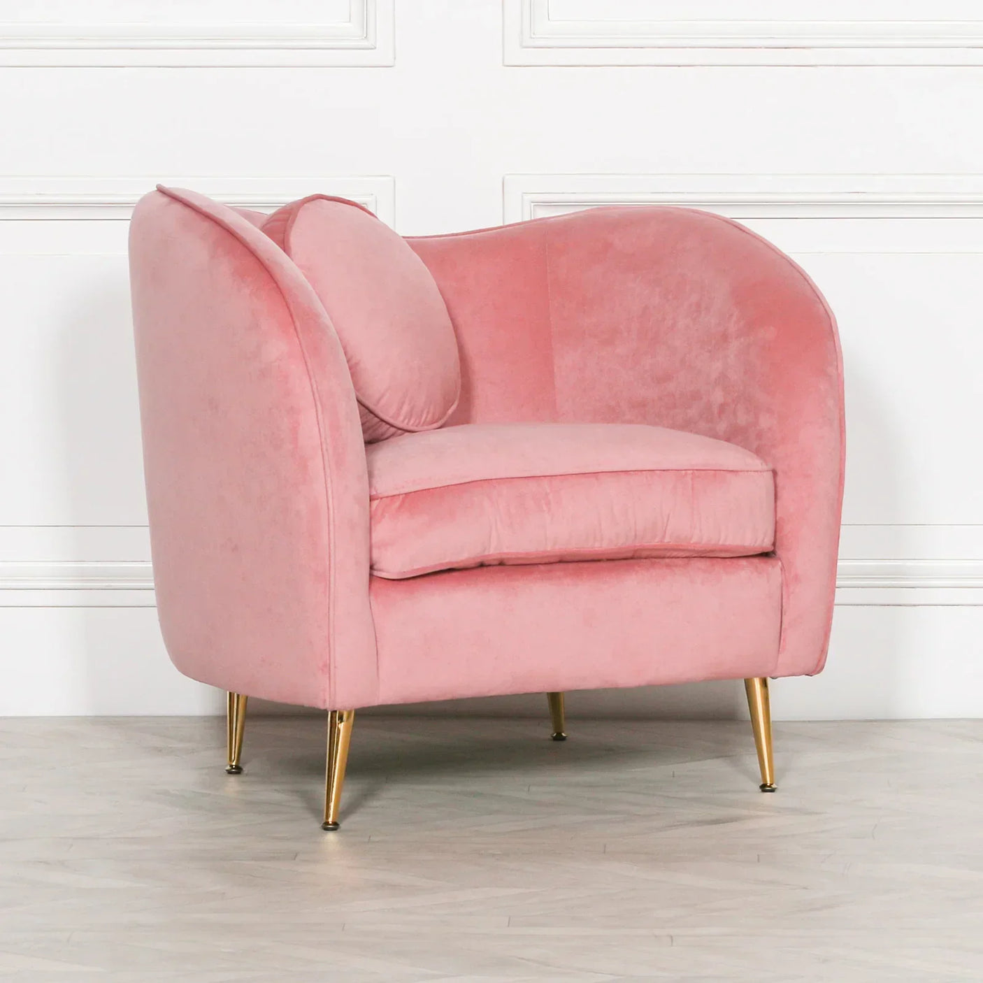 Pink velvet armchair with gold legs and matching round cushion in modern room