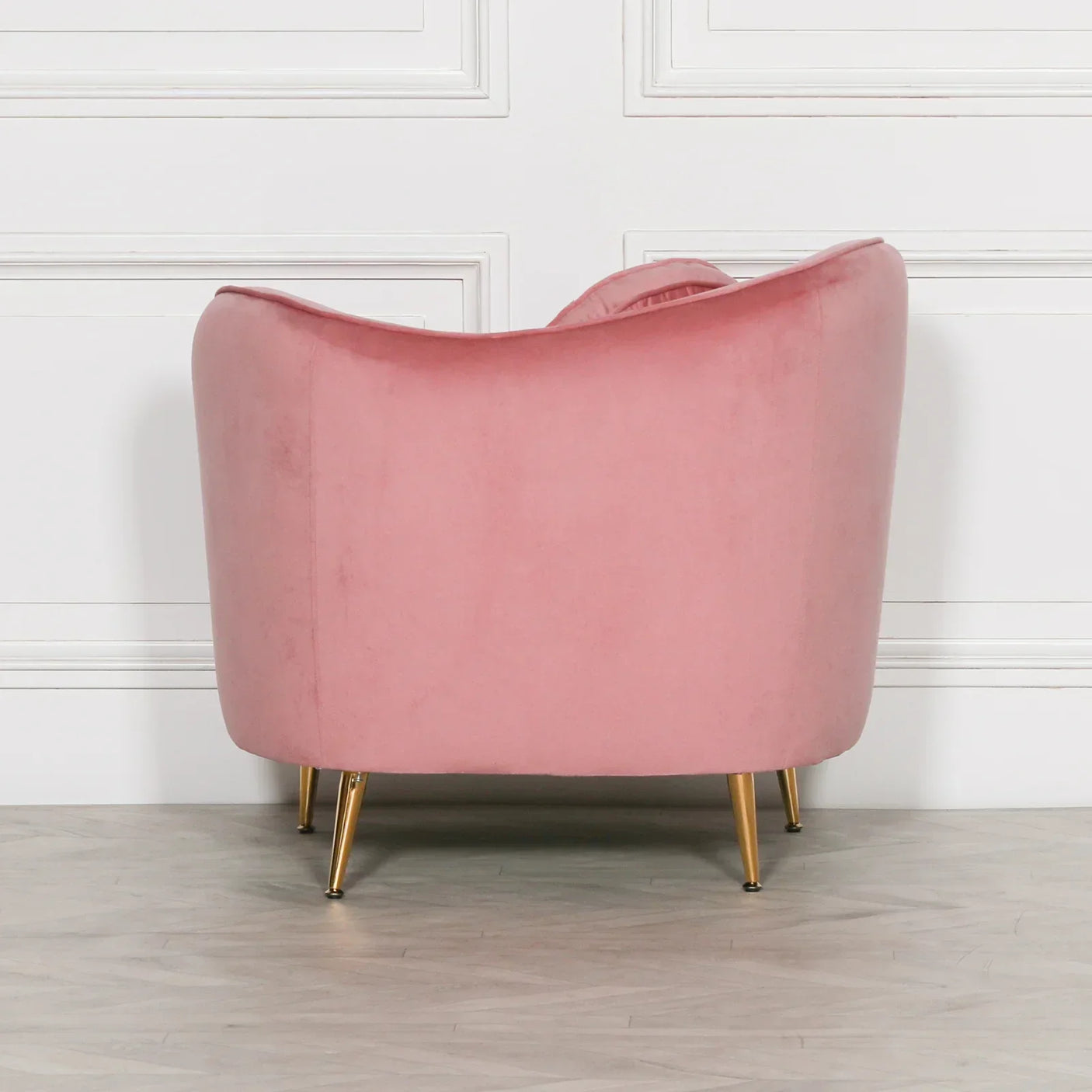 Back view of pink velvet accent chair with gold legs against white panelled wall