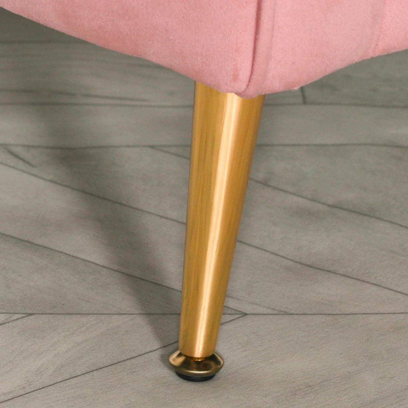 Close view of gold metal sofa leg with pink upholstery on grey tile floor