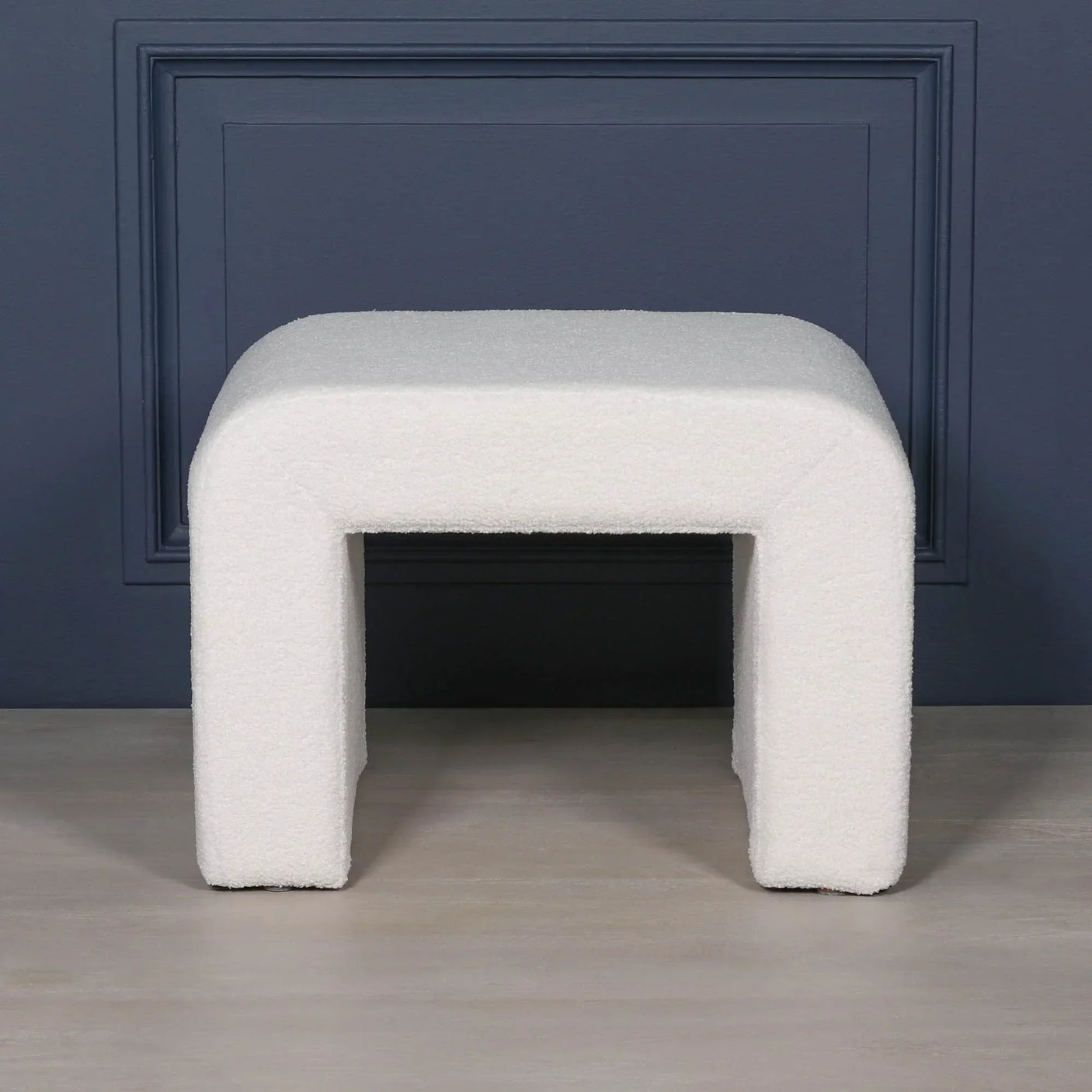 Curved white boucle upholstered bench with modern legs in front of navy wall panel
