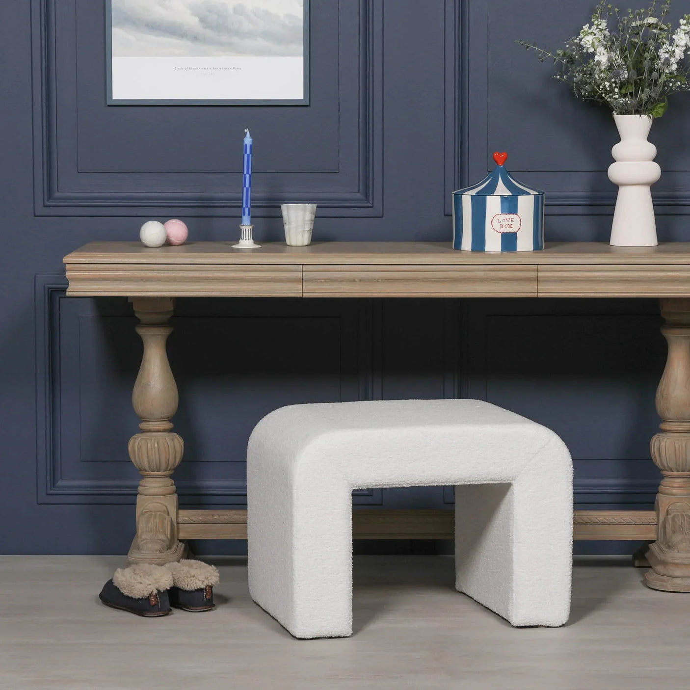 White boucle bench stool in front of wooden console table with decorative accents
