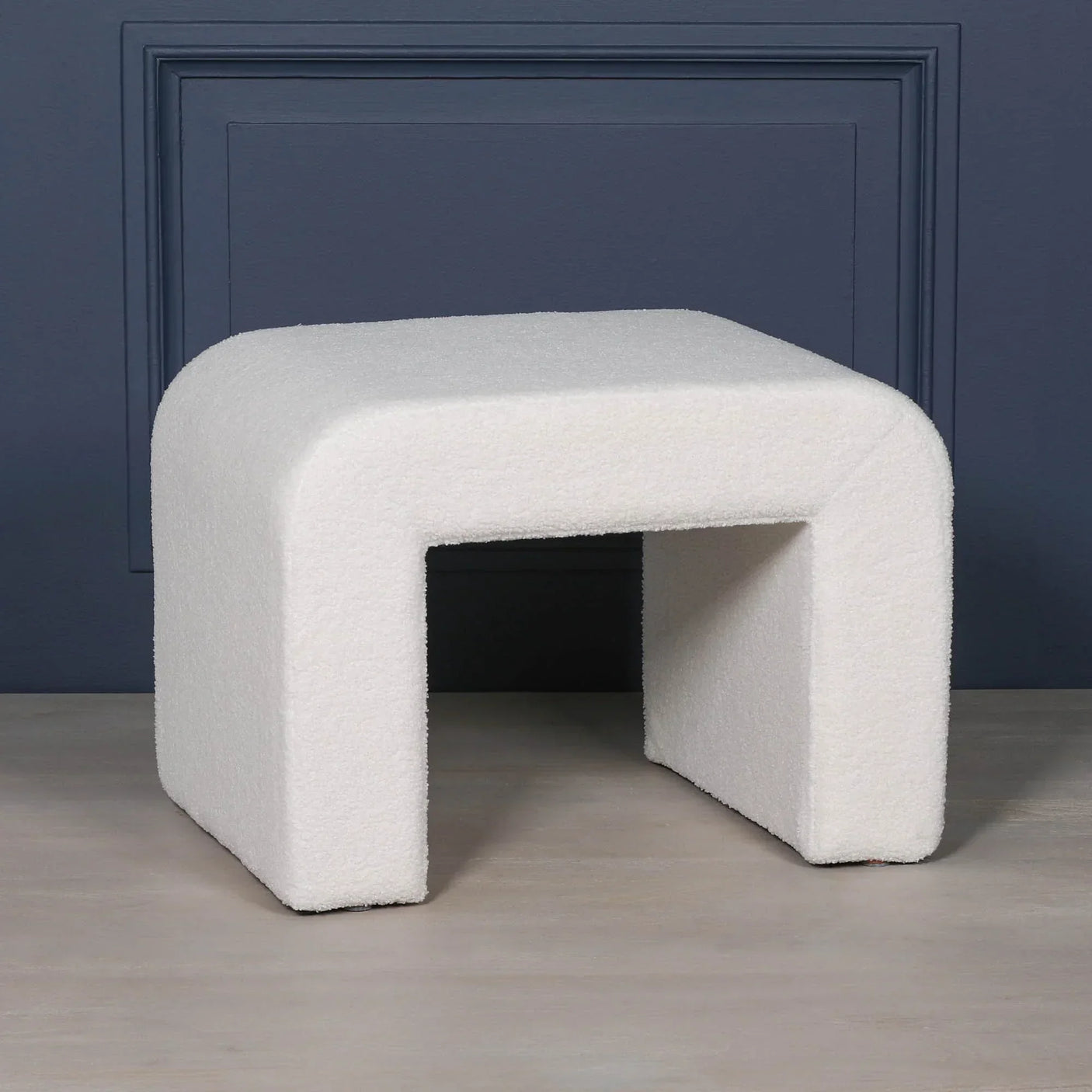 Modern white boucle ottoman bench with curved edges against blue wall