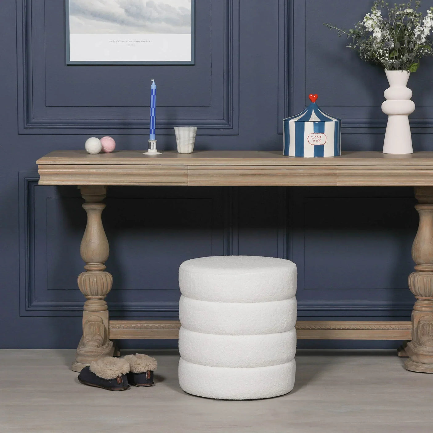 White boucle round ottoman stool in front of wooden console table with decorative items