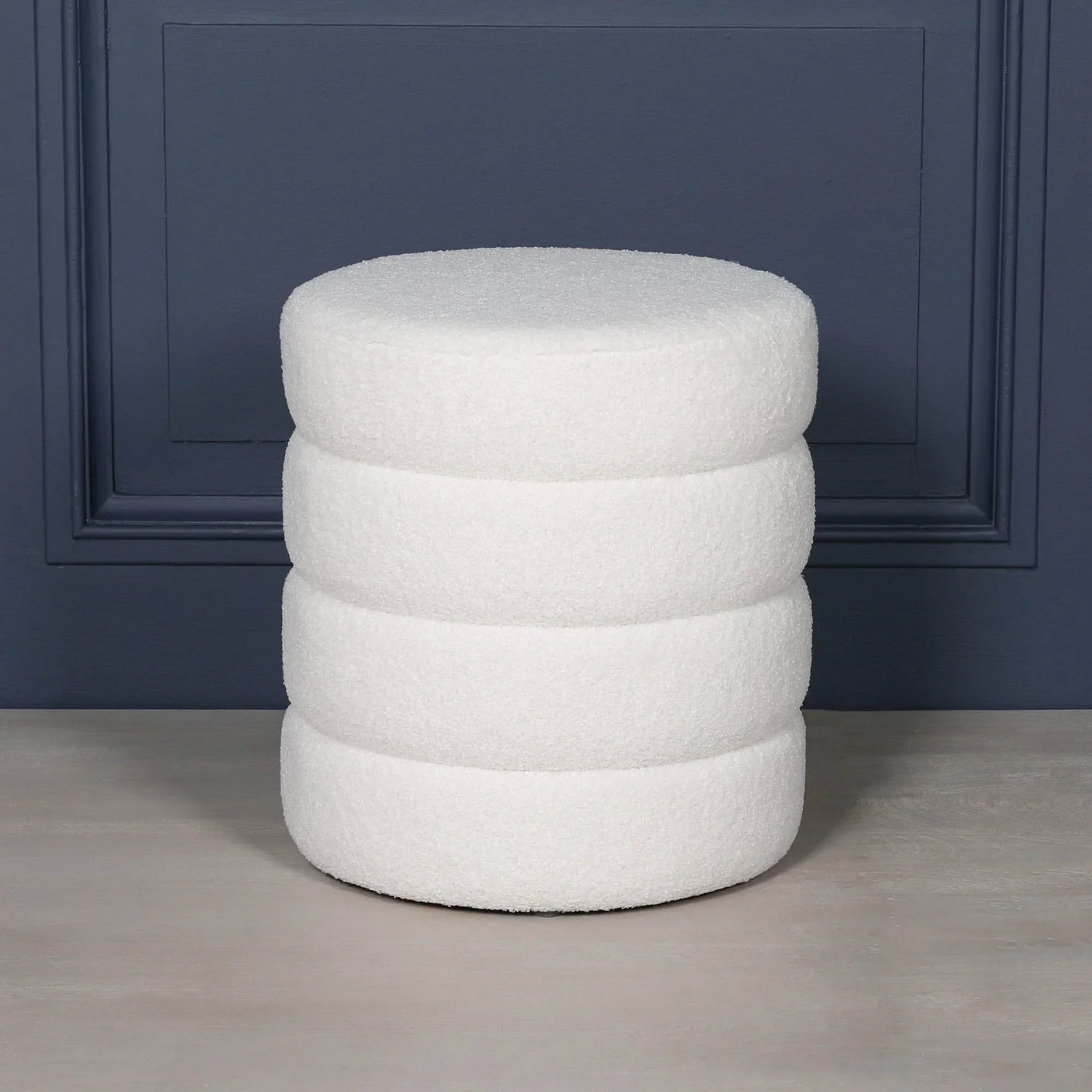 White boucle round footstool with stacked cushion design against blue wall