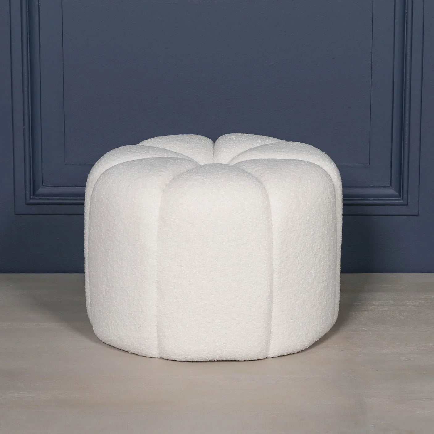 White boucle ottoman stool with scalloped edges against dark blue wall