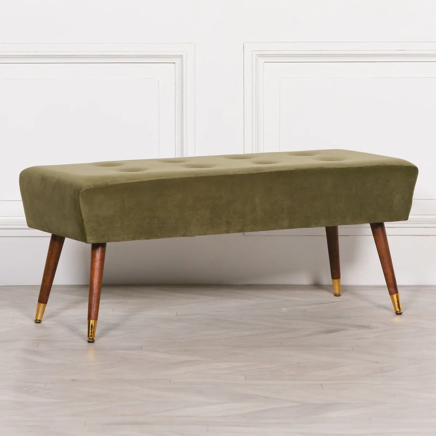 Olive green velvet bench with button-tufted seat and wooden legs with gold caps on hardwood floor