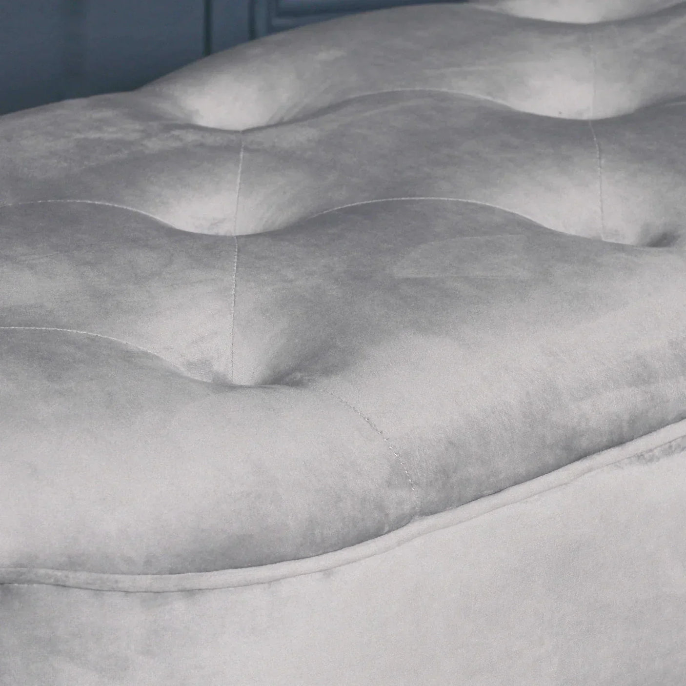 Close-up of grey velvet ottoman with tufted cushion detail