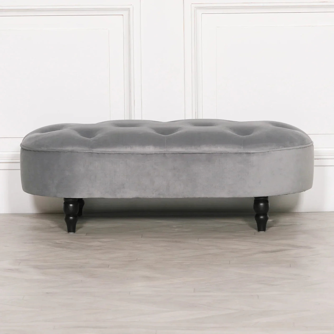 Grey velvet ottoman bench with button tufting and black wooden legs on wood floor