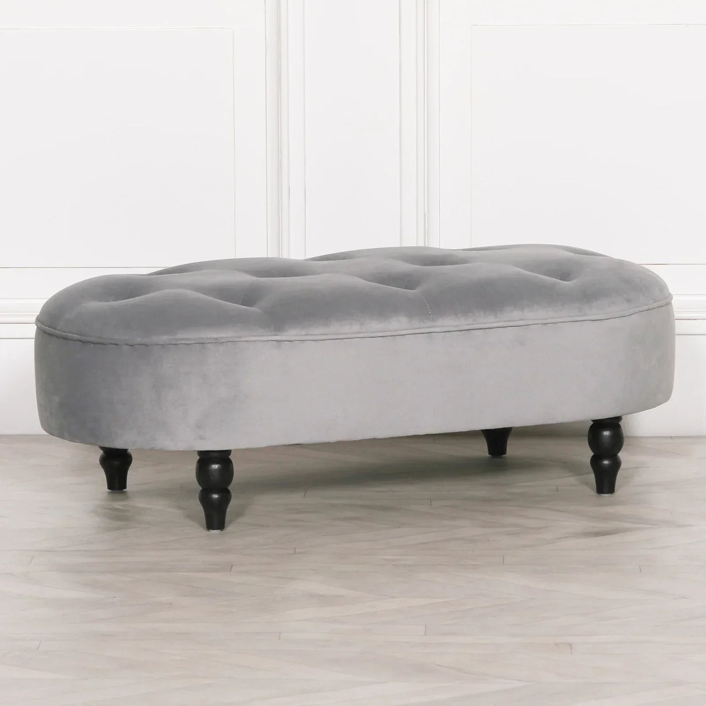 Grey velvet ottoman bench with button-tufted top and black turned wooden legs on wood floor