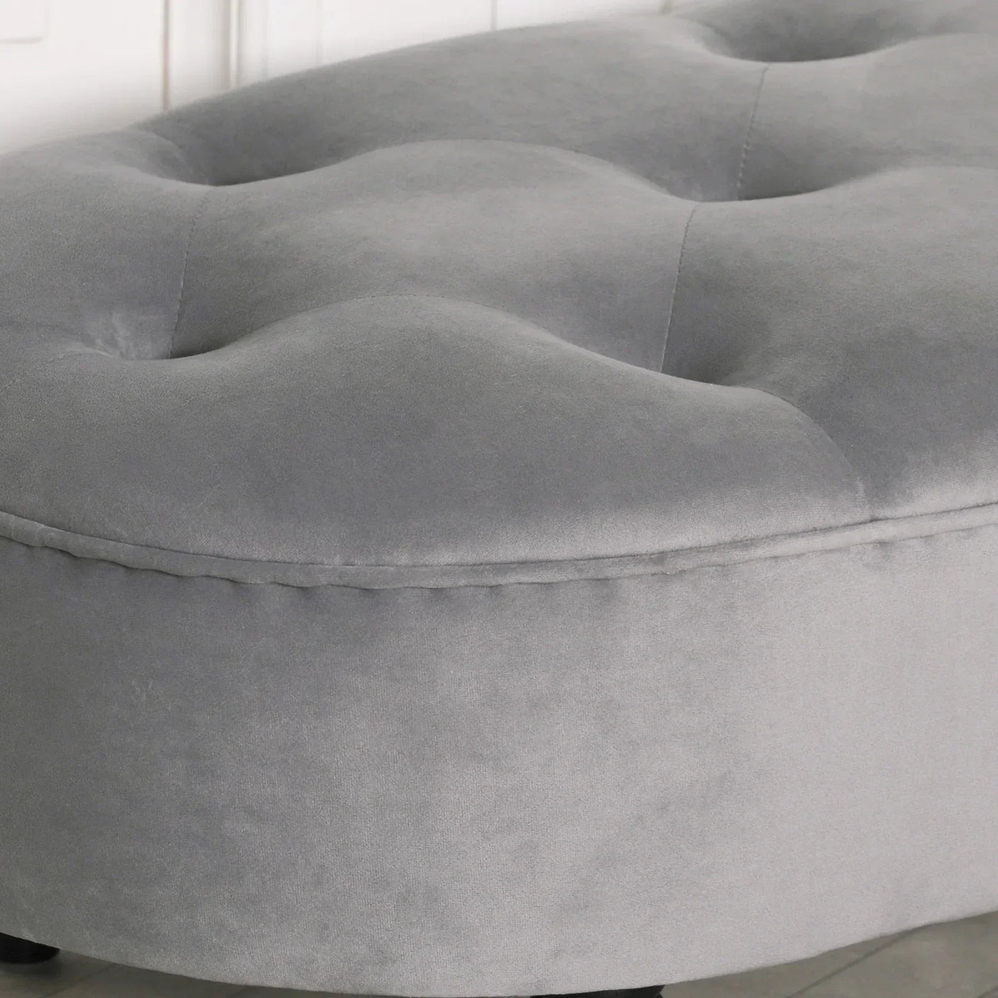 Grey velvet upholstered ottoman with tufted top, close-up side view