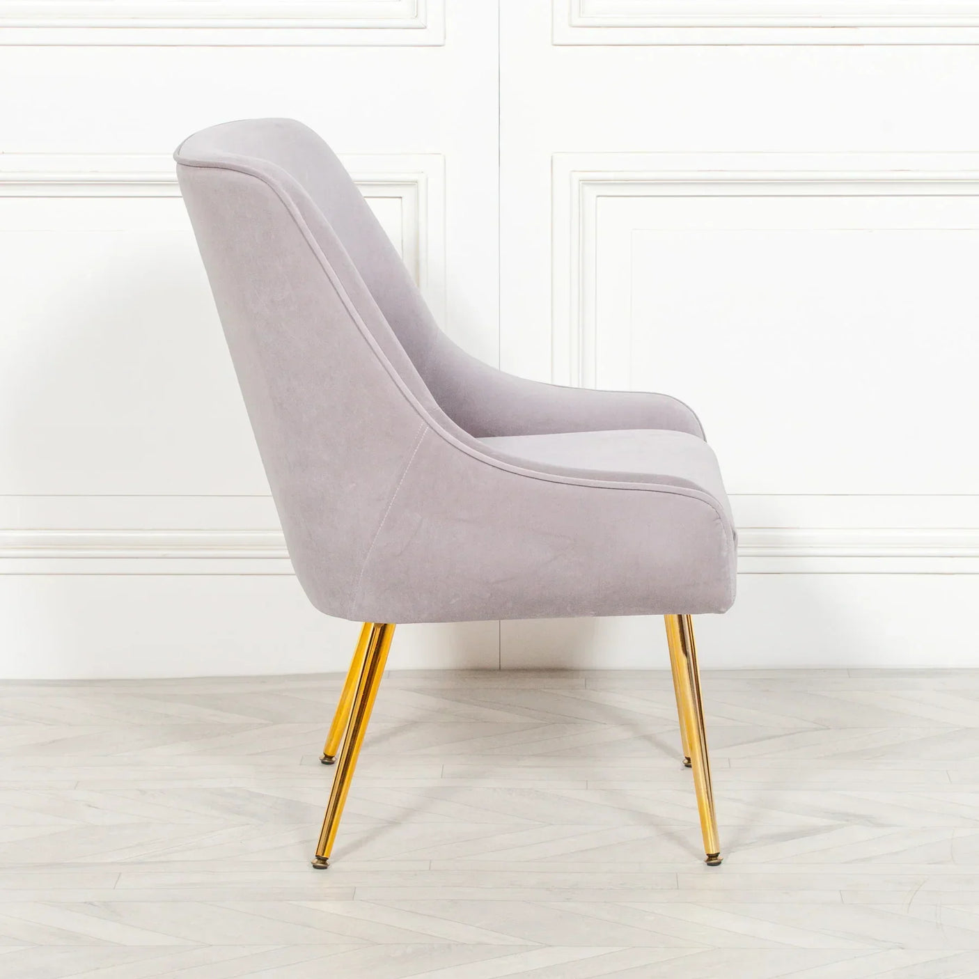 Side view of grey accent chair with gold metal legs on light wood floor
