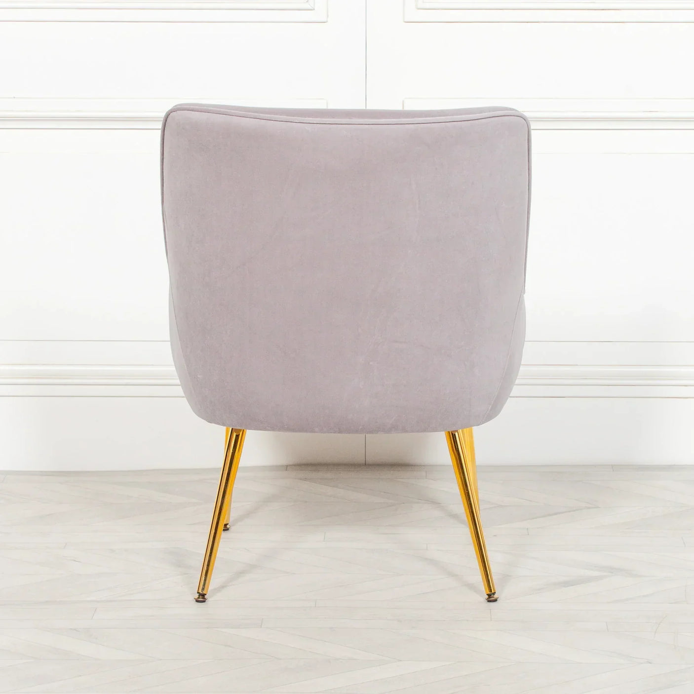 Grey accent chair with gold metal legs rear view against white panelled wall