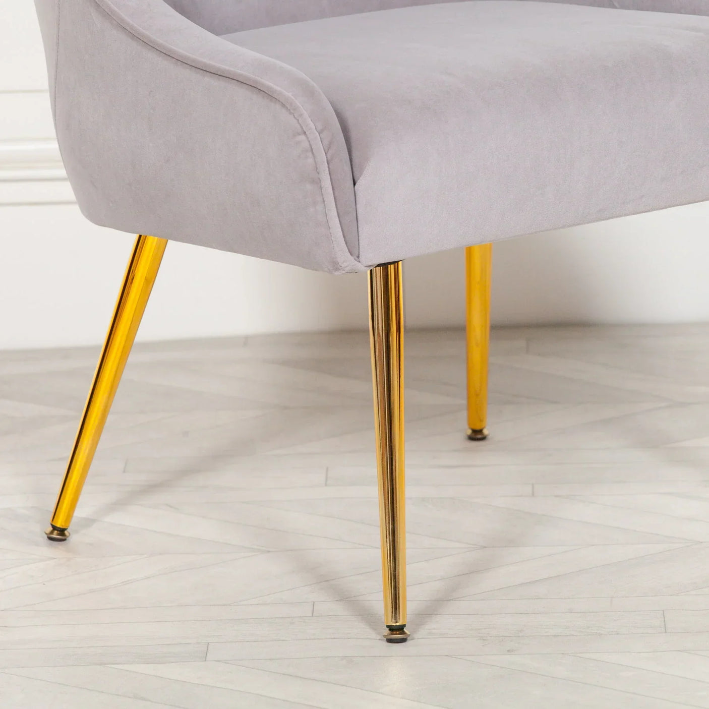 Grey fabric accent chair with gold metal legs on light herringbone wood floor