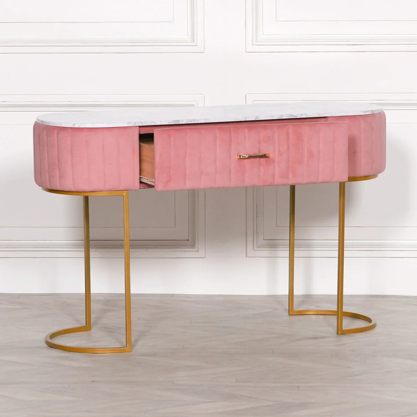 Pink velvet console table with marble top, gold legs, and open drawer against a white wall