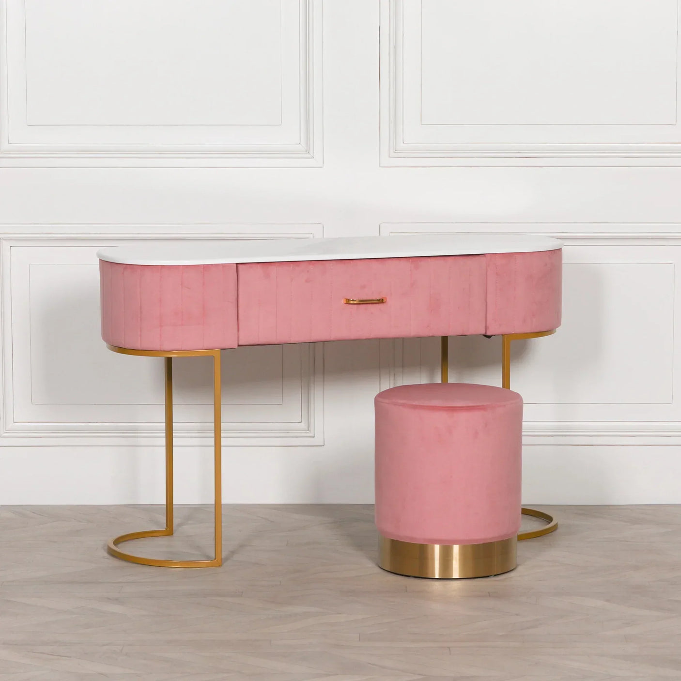 Pink velvet dressing table with gold legs and matching round stool on light wood floor