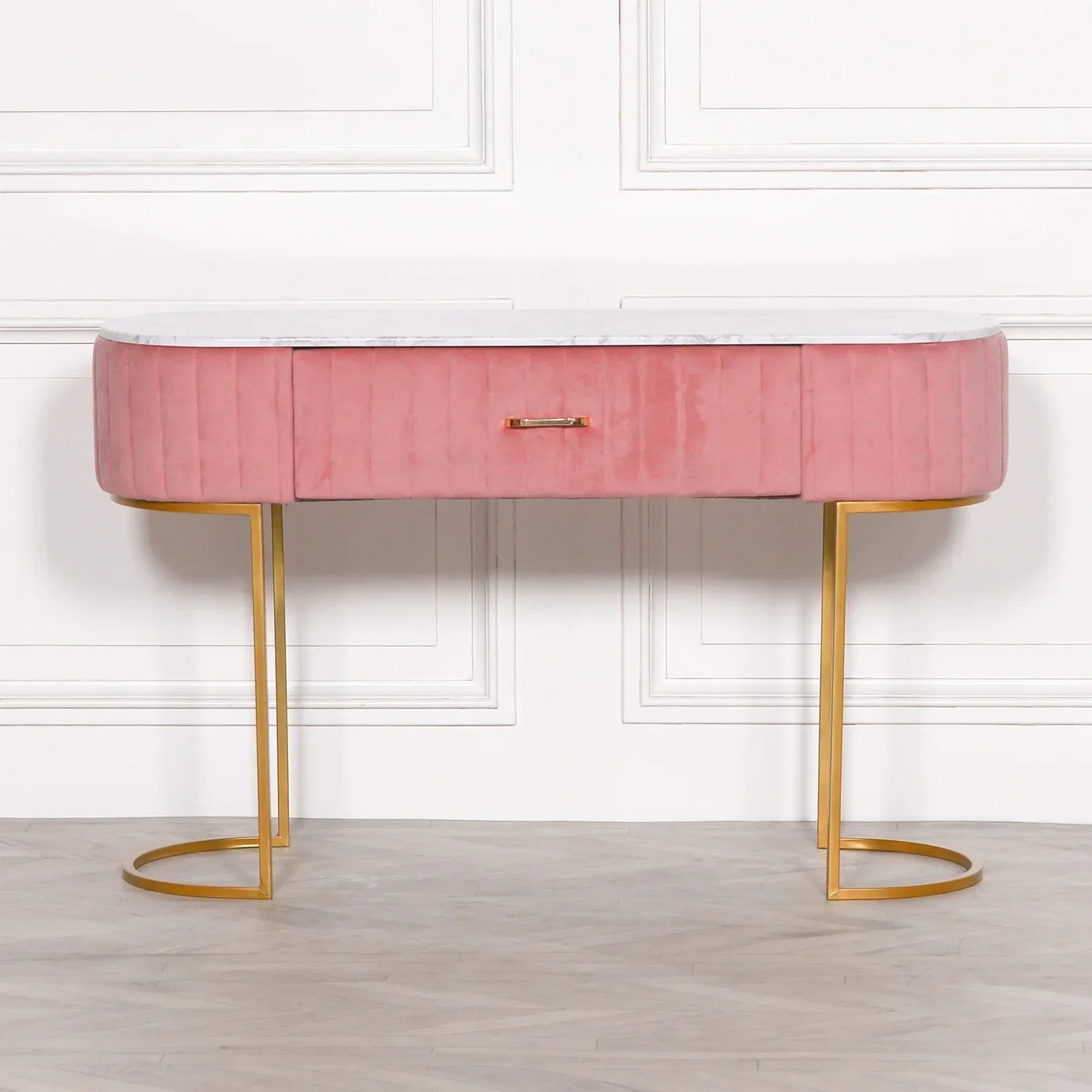 Pink velvet console table with gold metal legs and white marble top against a white wall