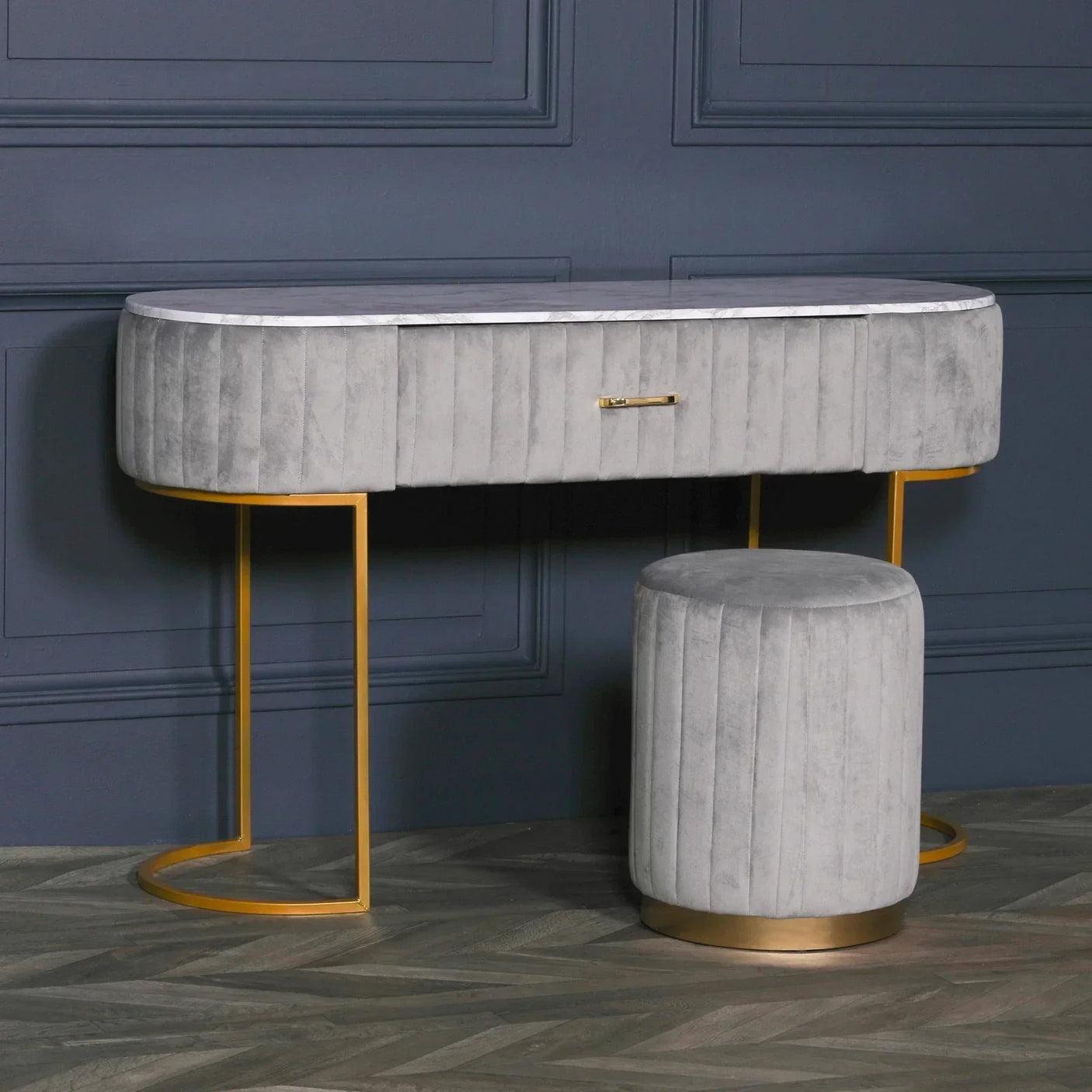 Grey velvet dressing table with gold legs and matching round stool against dark wall