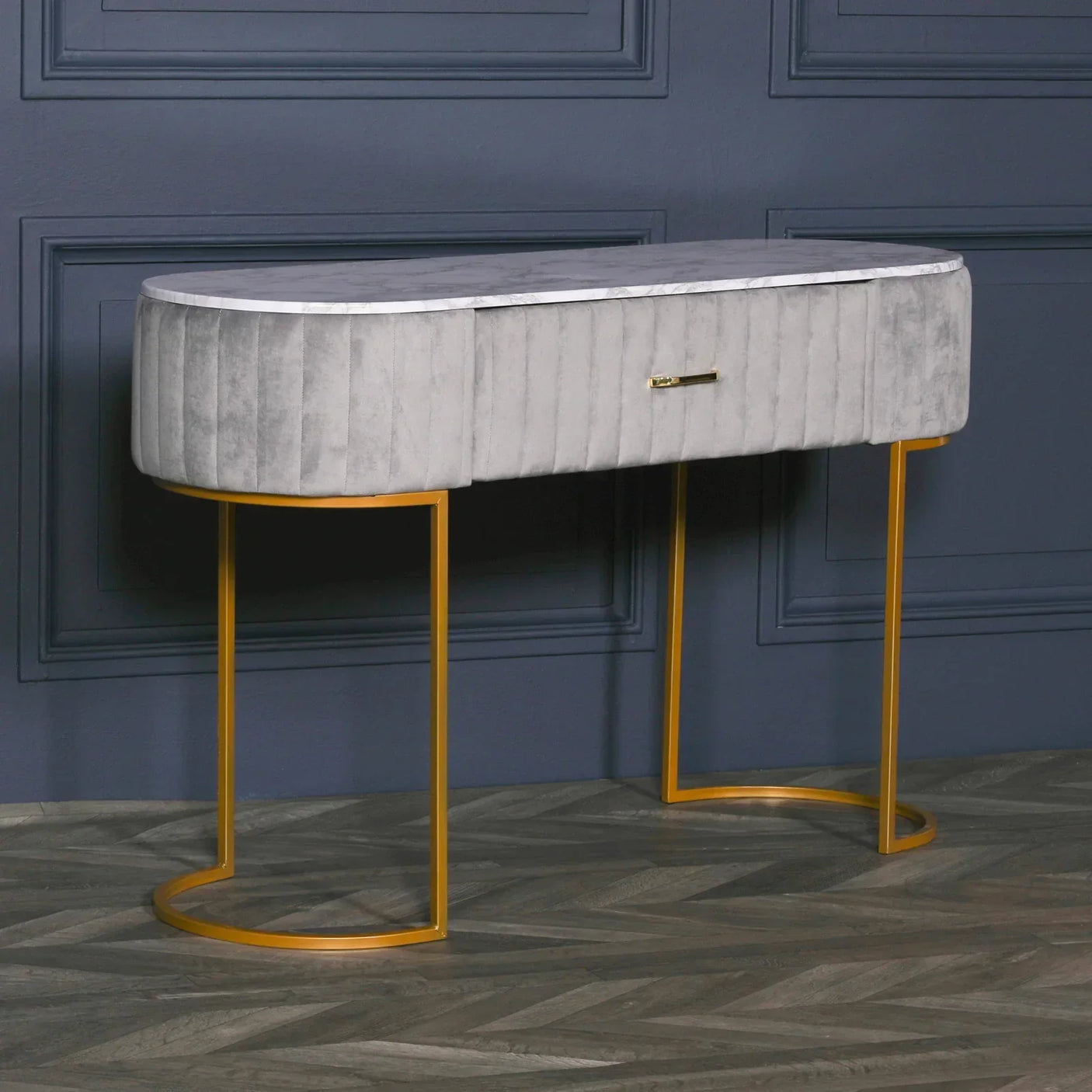 Grey velvet console table with gold metal legs and marble top against dark wall