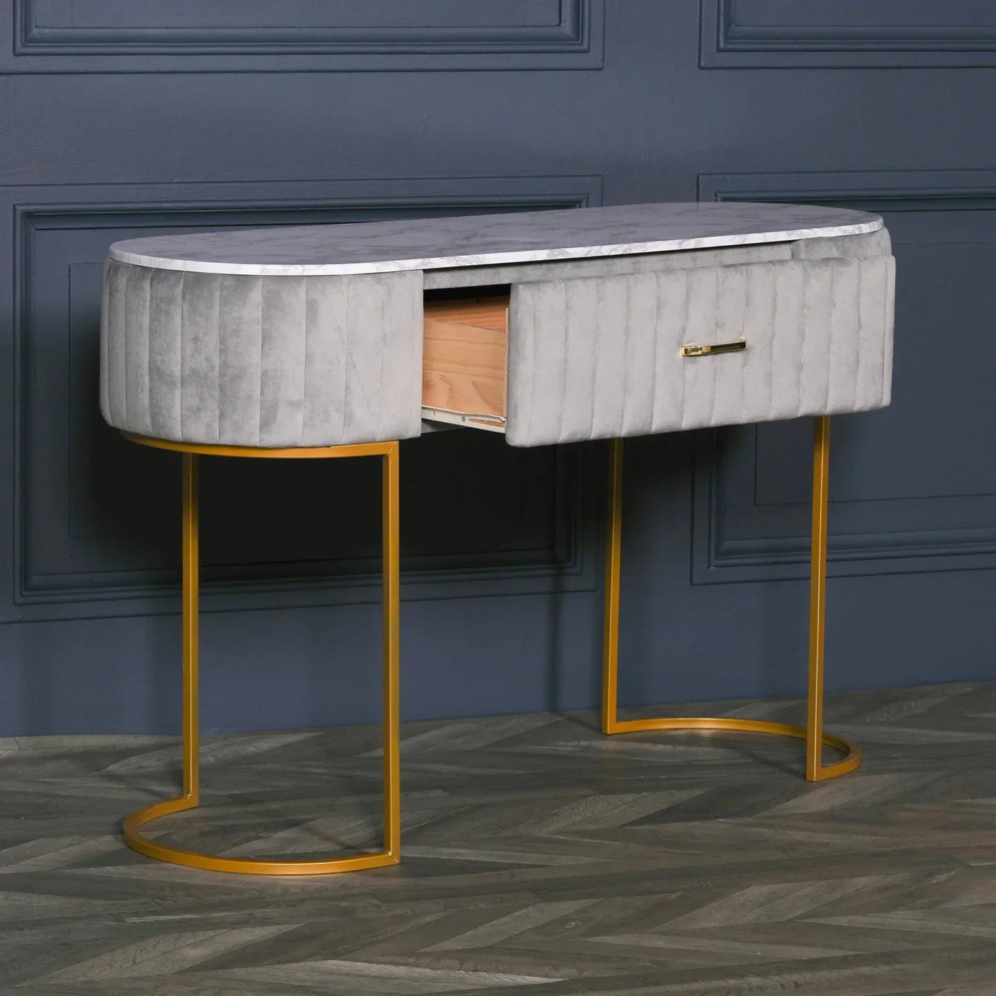 Grey velvet console table with gold legs and open drawer against blue wall