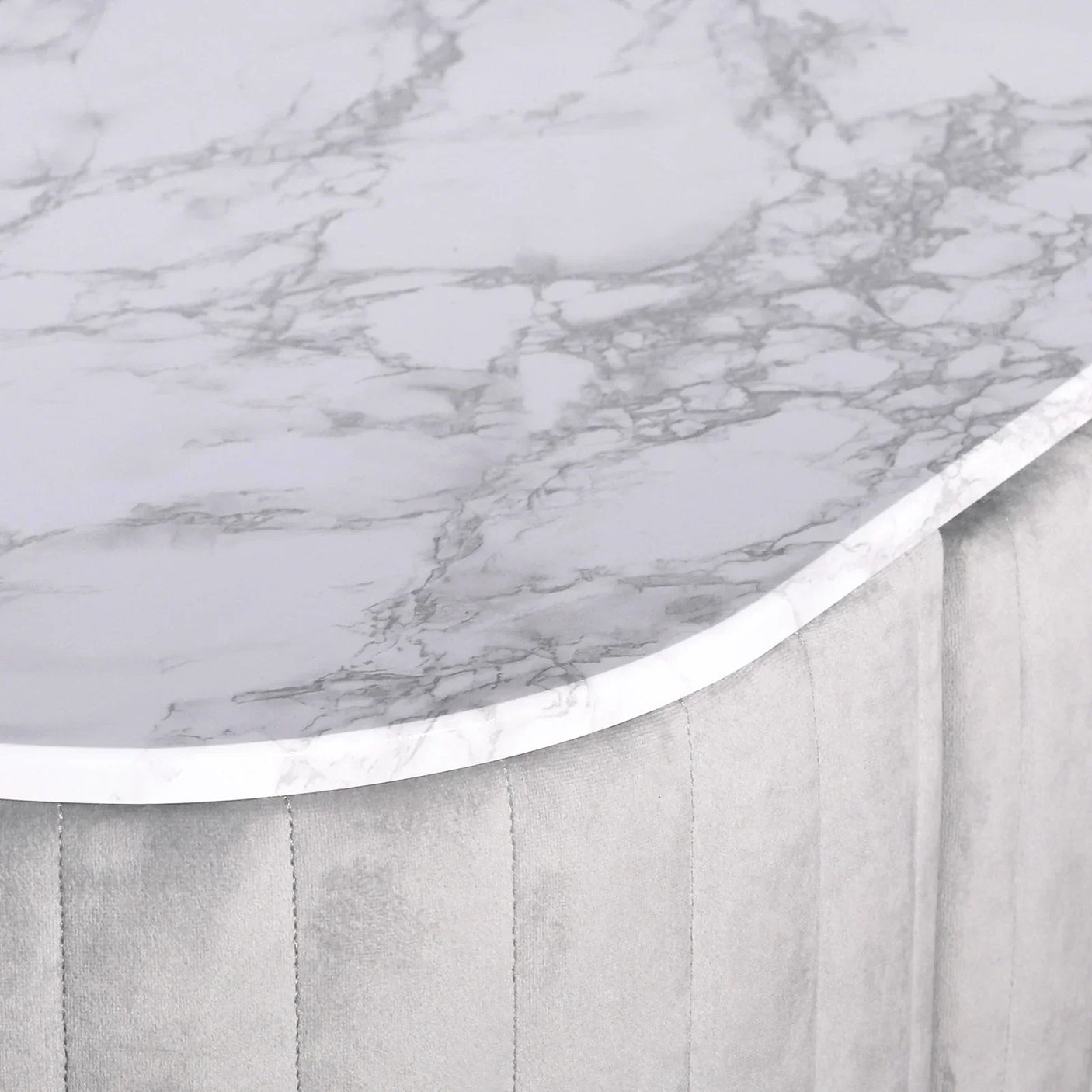 Round marble top coffee table with grey upholstered base, close-up corner view